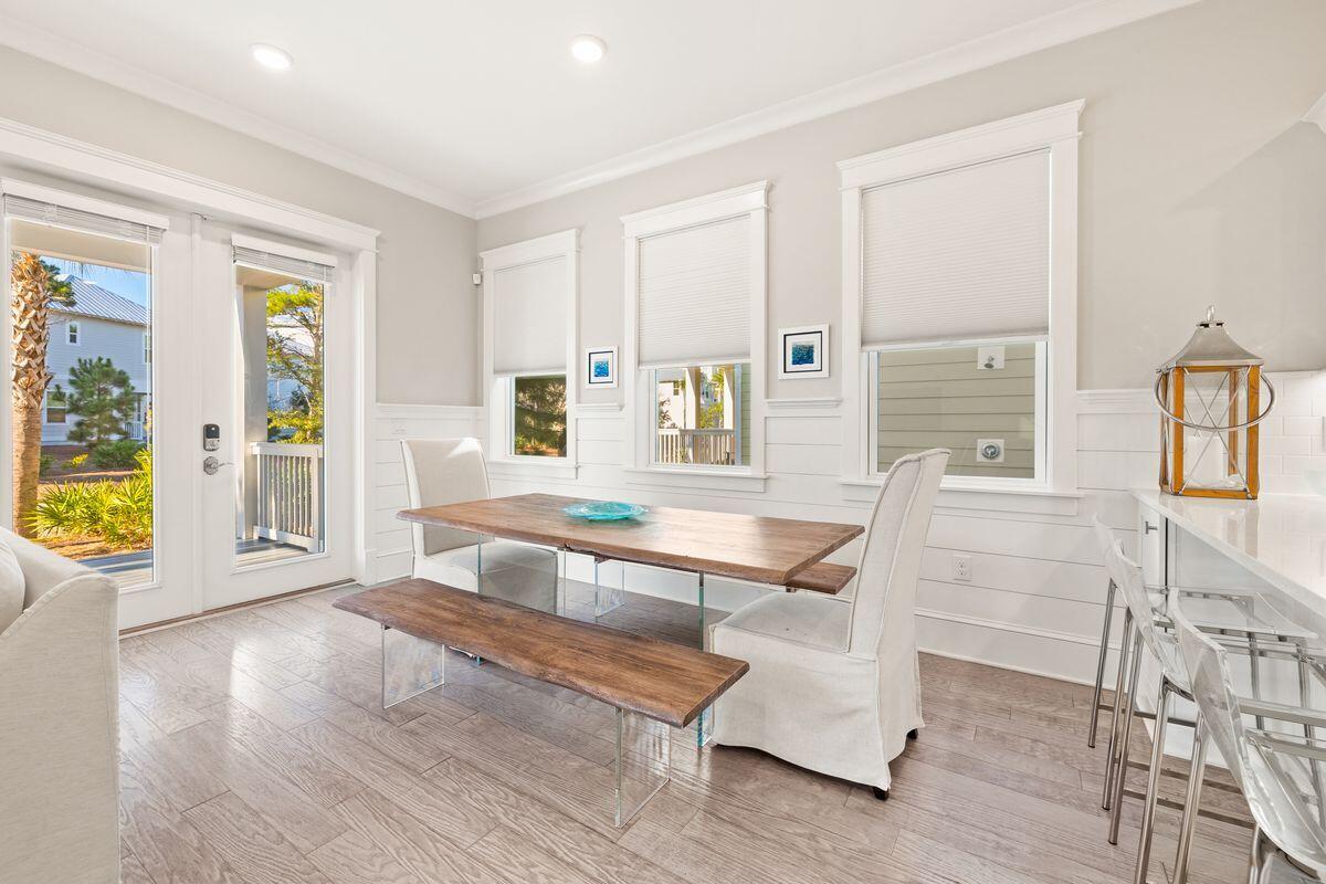 Dining area with a wood table and bench, white chairs, and tall windows beside a glass porch door.