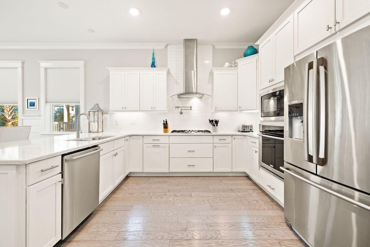 Bright white kitchen with stainless steel appliances, a gas cooktop, and a foreground peninsula.
