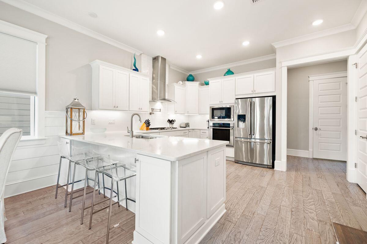 White kitchen with a large island, clear bar stools, and stainless steel appliances.