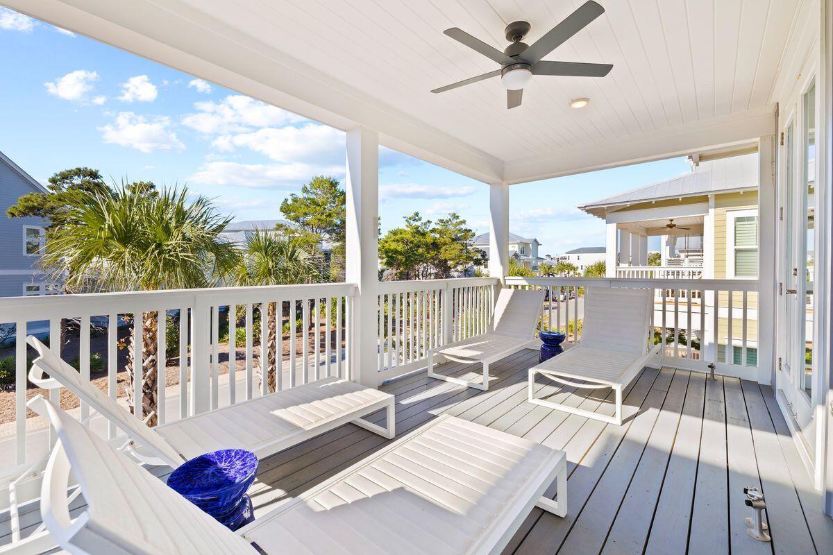 Covered deck with white lounge chairs and a ceiling fan, overlooking palm trees and neighboring homes.