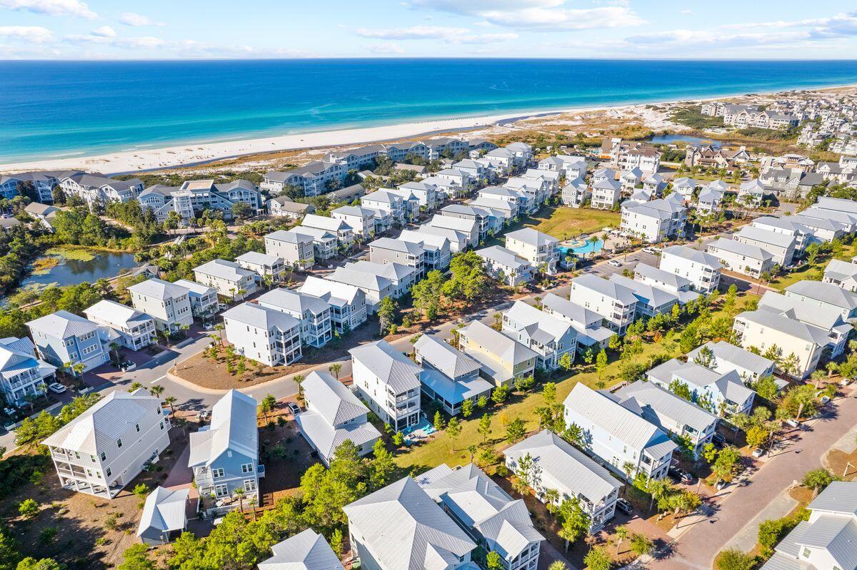 Aerial coastal neighborhood of light-colored homes beside a sandy beach and turquoise water.