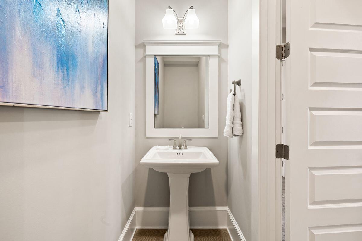 Bathroom with a white pedestal sink, framed mirror, blue abstract art, and open paneled door.