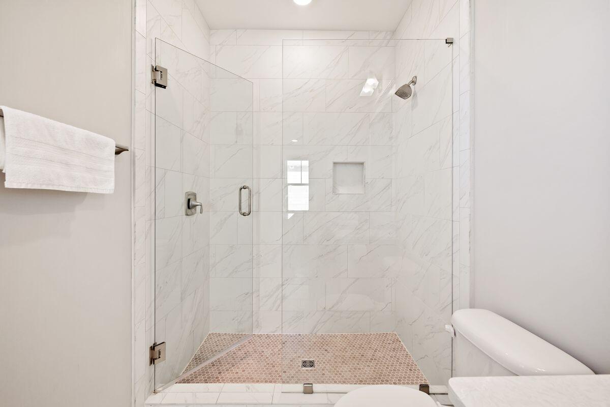 Bathroom with a glass-enclosed marble-look shower and hexagonal mosaic floor.