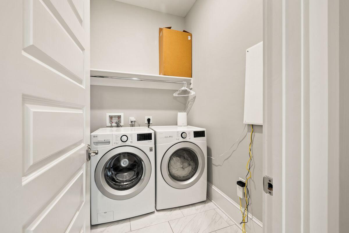 Laundry room with side-by-side front-loading washer and dryer beneath a shelf with hangers.