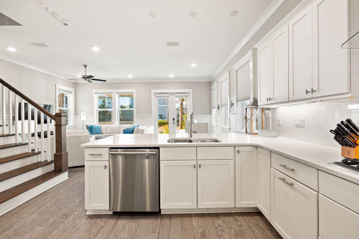 Bright white kitchen with a quartz island, stainless-steel dishwasher, and open view to the living room.