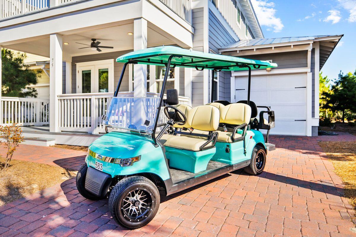 Gray coastal-style house with covered porch and garage, fronted by a turquoise golf cart on a brick driveway.