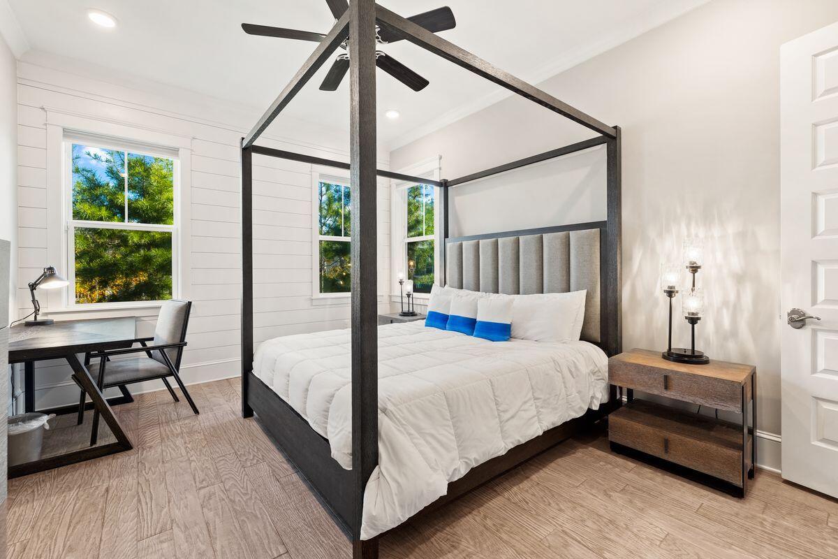 Bedroom with a dark four-poster bed, blue accent pillows, and windows overlooking greenery.