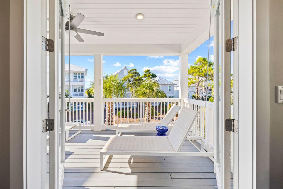 Covered porch with white chaise lounges, ceiling fan, and views of neighboring homes and palm trees.