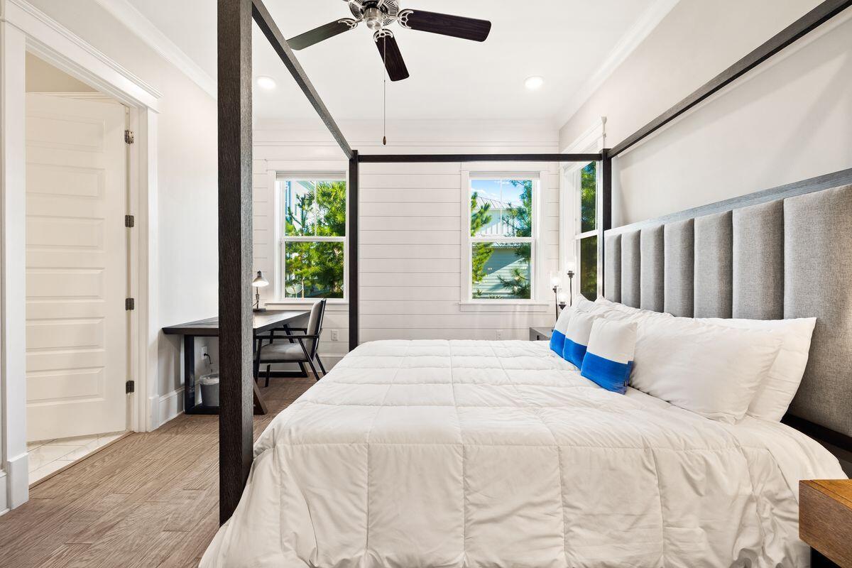 Bedroom with a dark four-poster bed, gray upholstered headboard, and desk beside two windows.