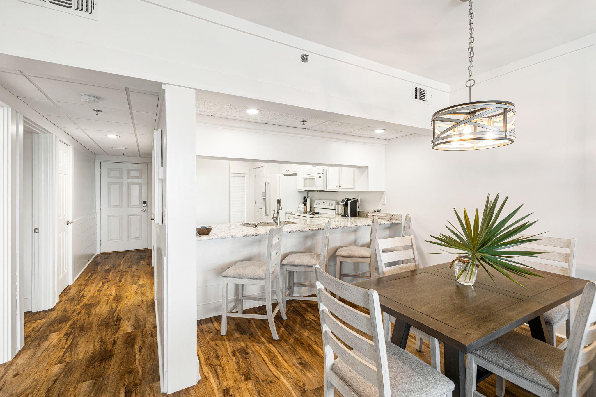 Dining area with a dark wood table beside a white kitchen and breakfast bar.