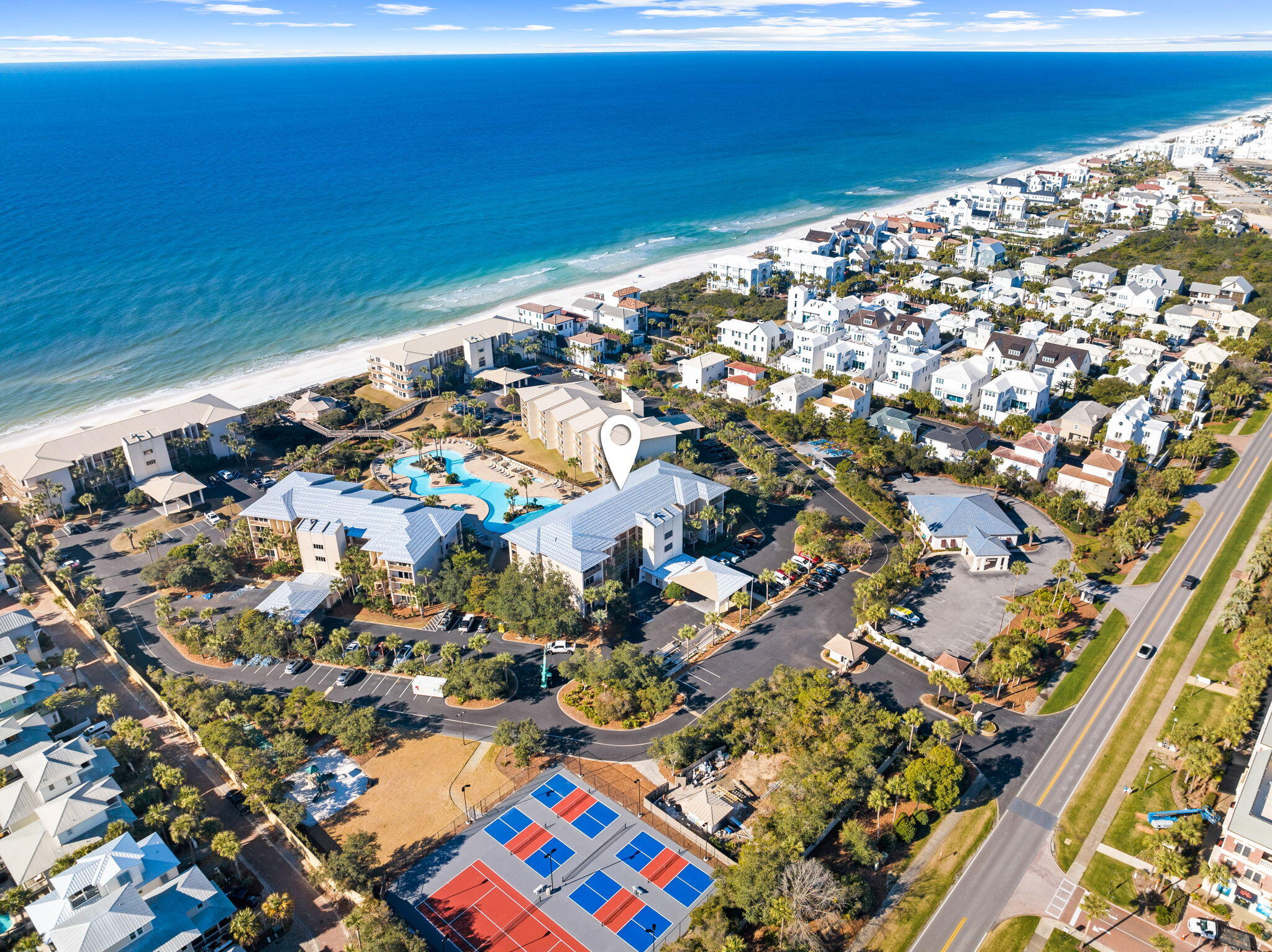 Coastal residential community with a winding pool, tennis courts, sandy beach, and ocean.