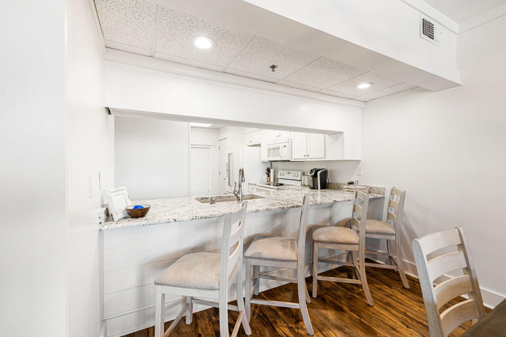 White kitchen with granite breakfast bar, upholstered stools, and dark wood floors.