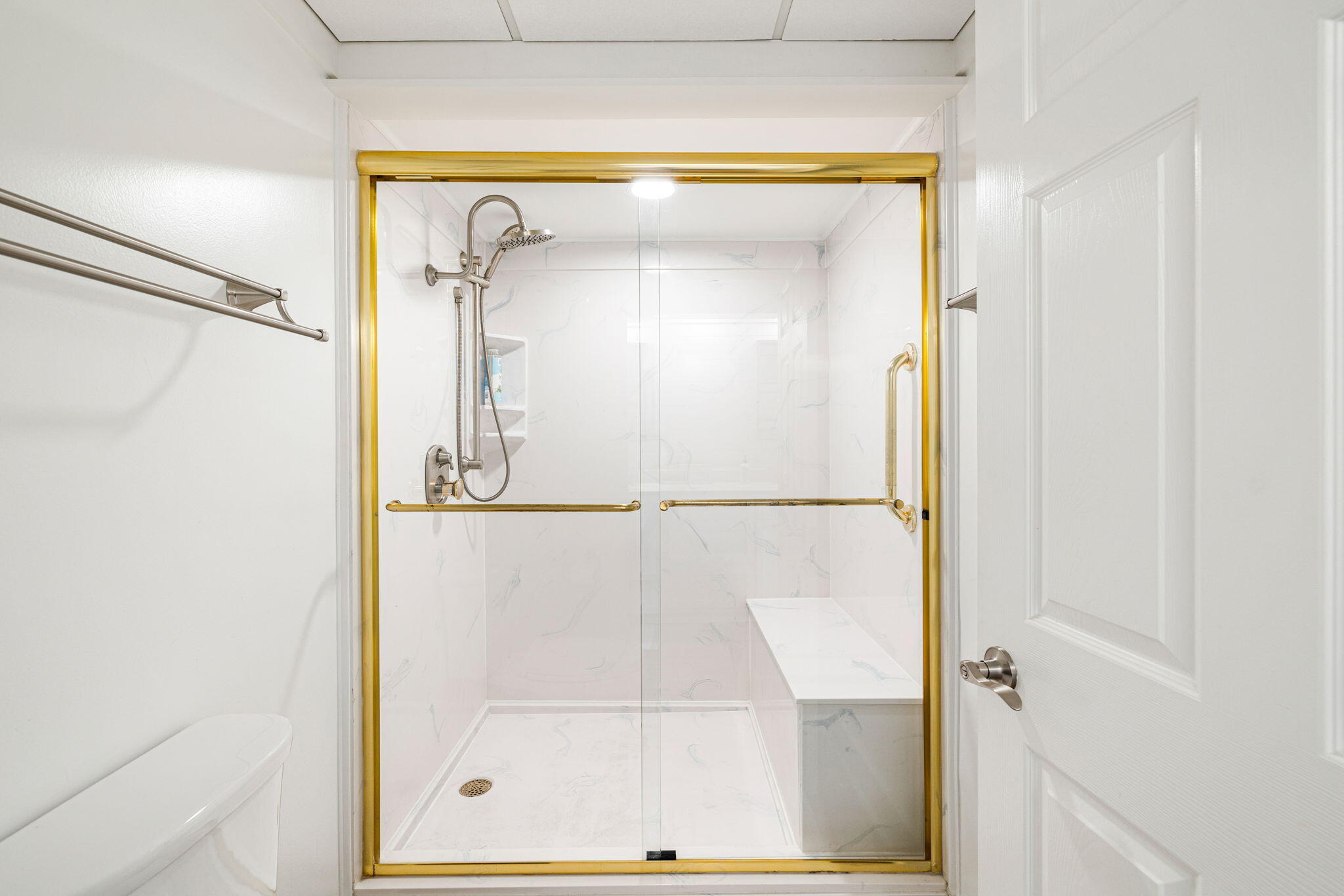 Bathroom walk-in shower with gold-toned glass framing, marble-look tile, and a built-in bench.