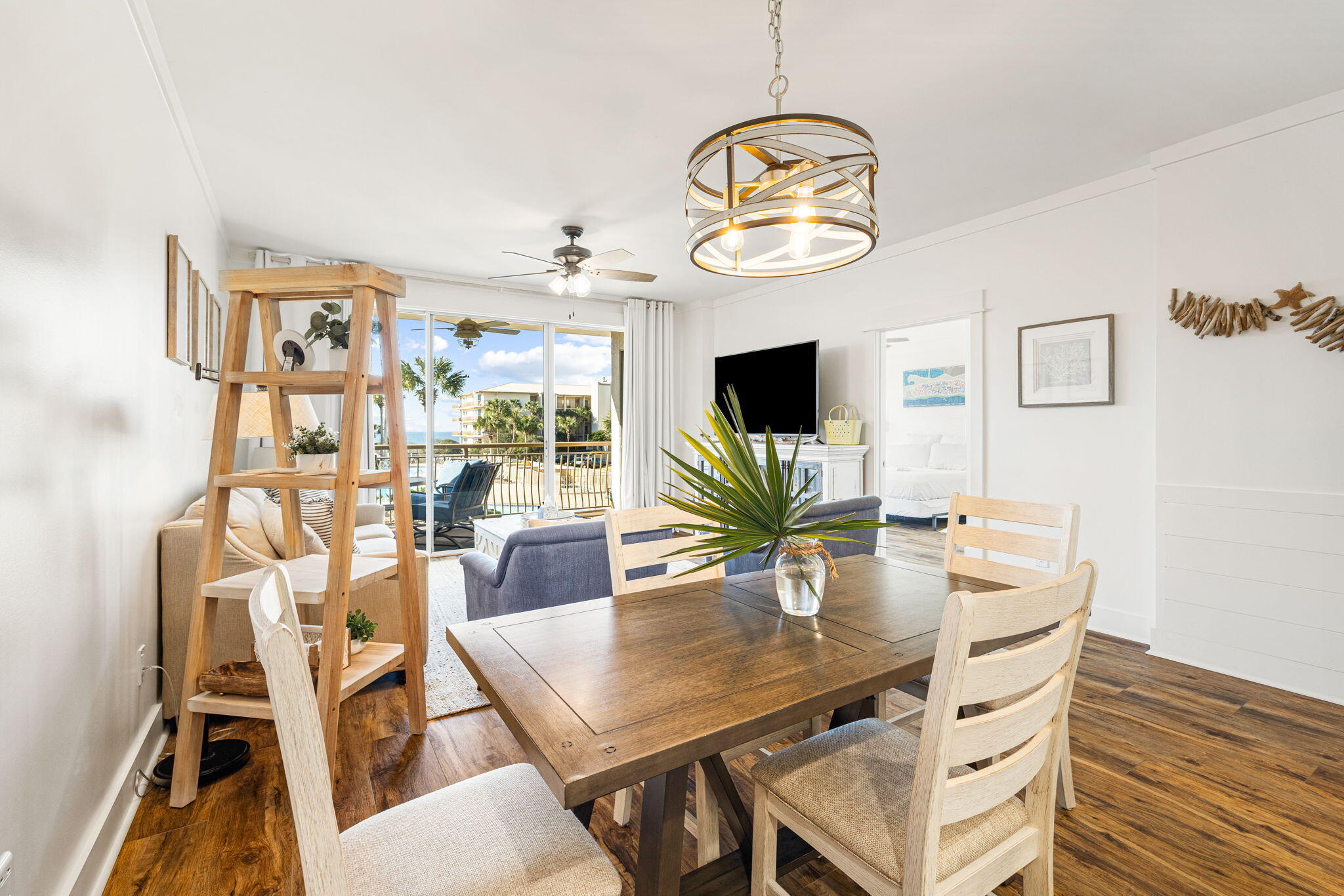 Staged condo dining area with a wood table, sofa, and balcony doors overlooking the coast.