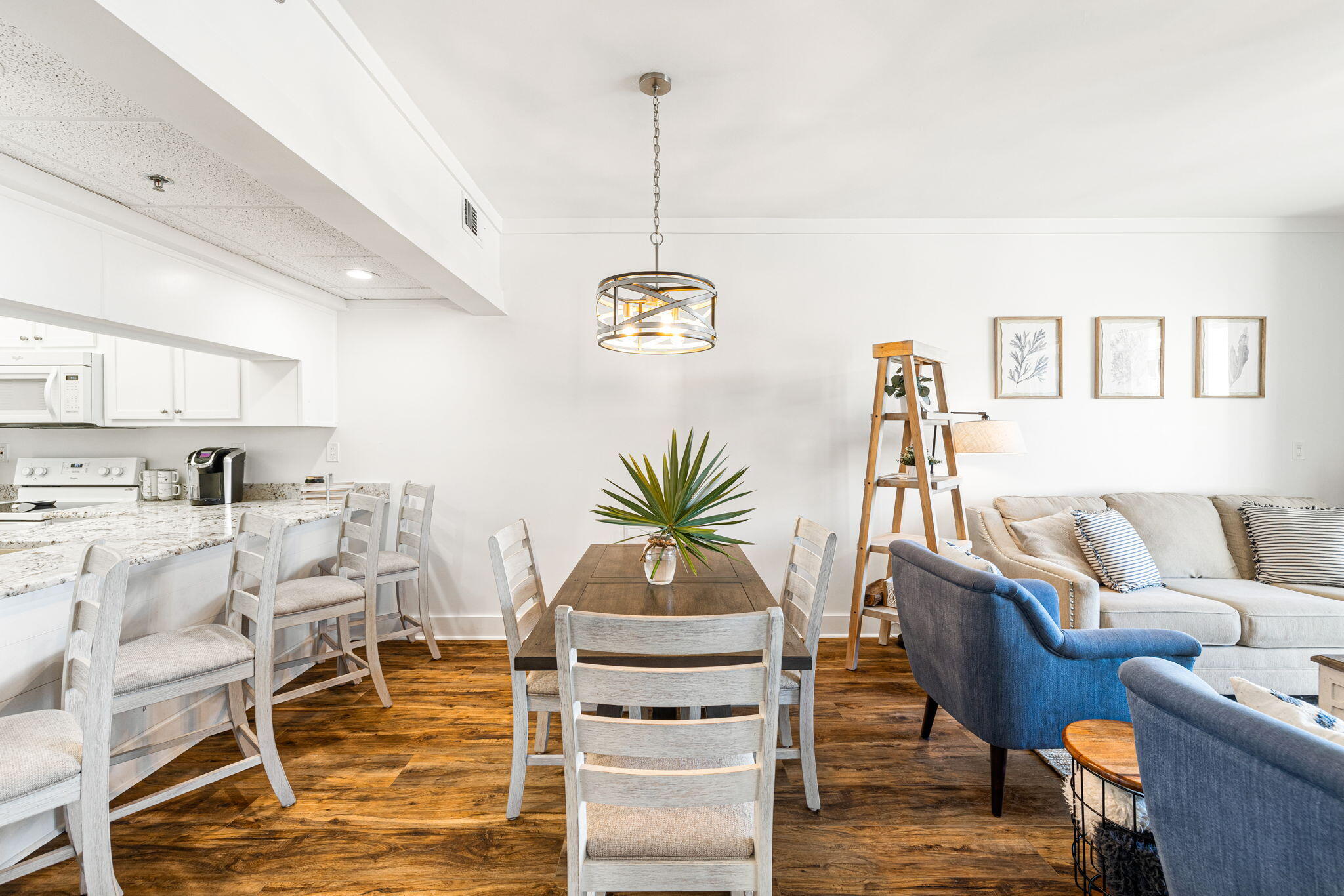 Open-plan condo living and dining area with a white kitchen, dark wood floors, and blue armchairs.
