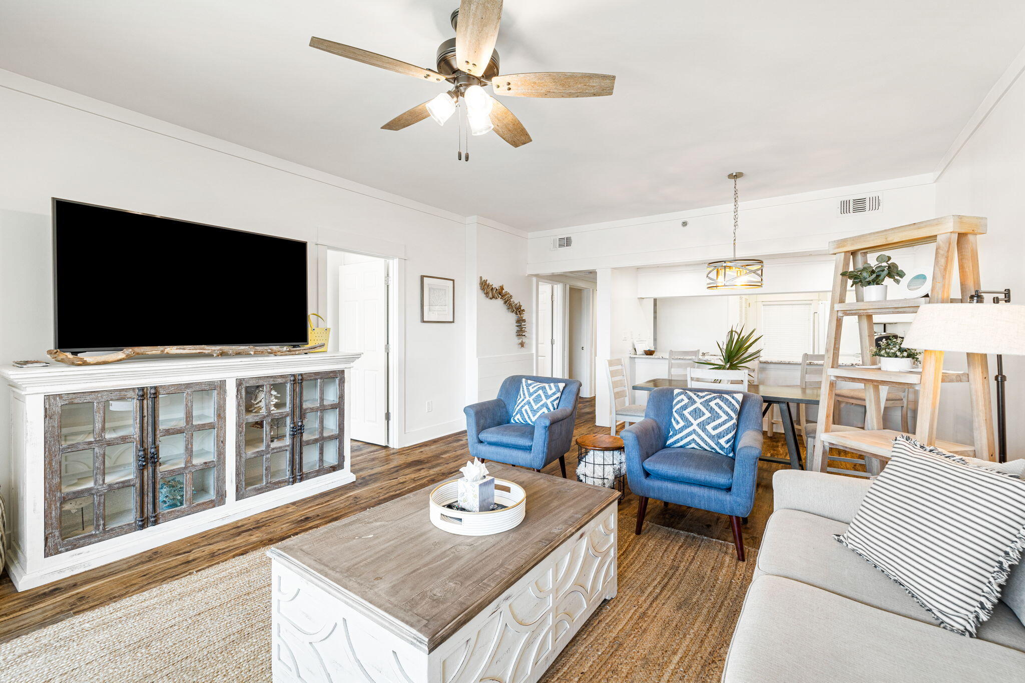 Furnished living room with blue armchairs, a rustic media cabinet, and an adjoining dining area.