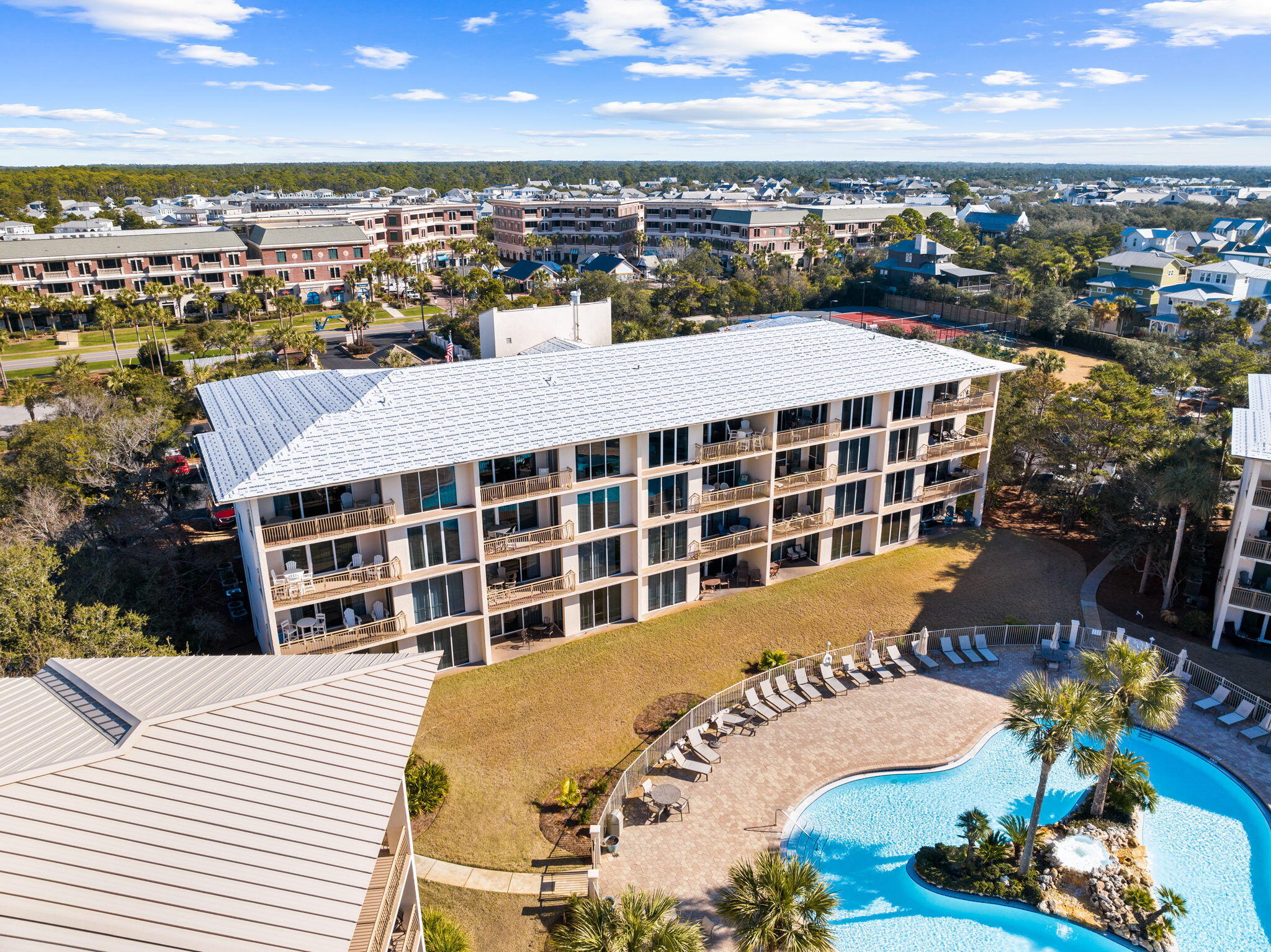 Aerial view of a condominium building beside a curved swimming pool and landscaped courtyard.