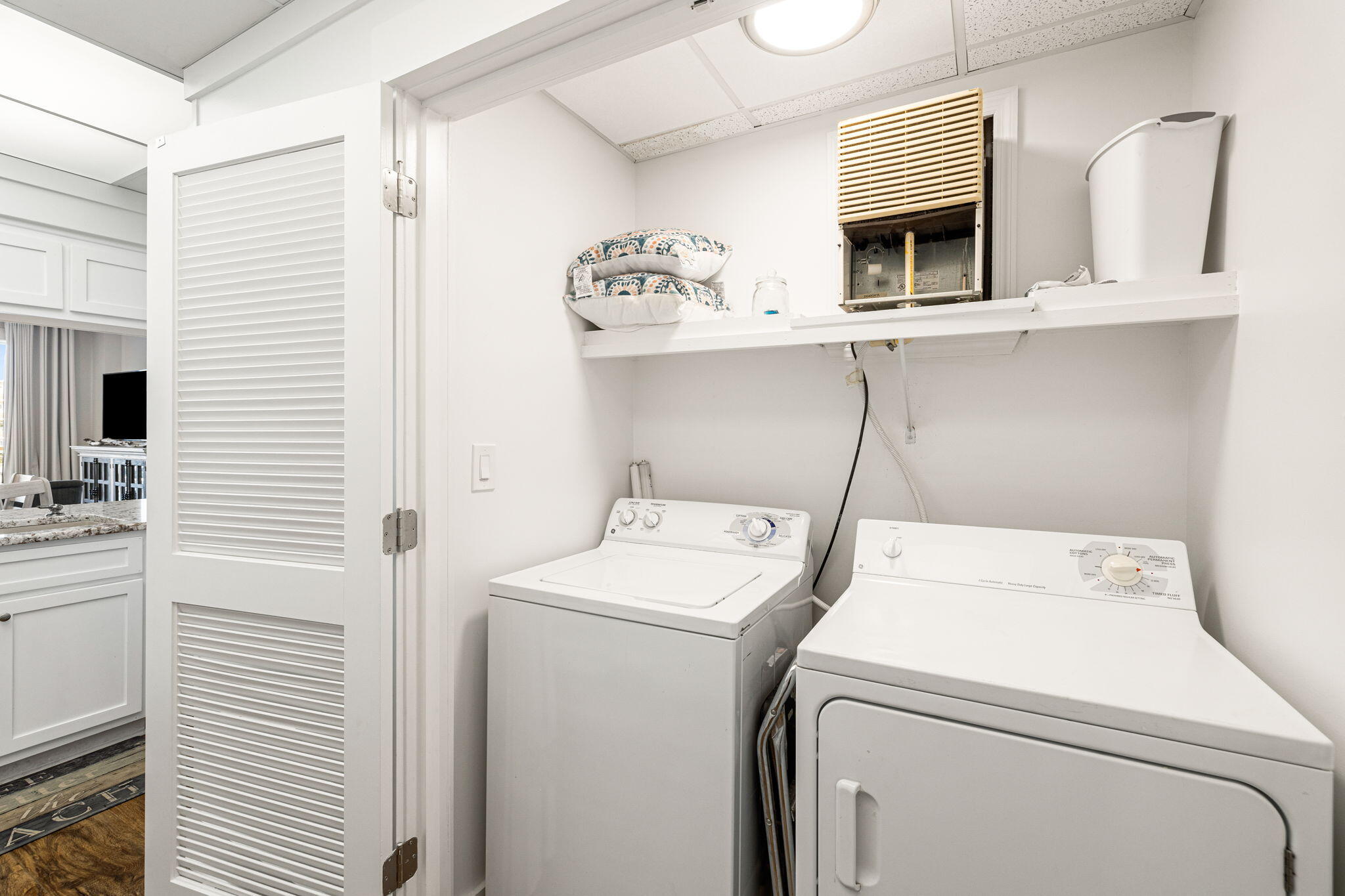 Laundry room with a top-loading washer, front-loading dryer, and storage shelf.
