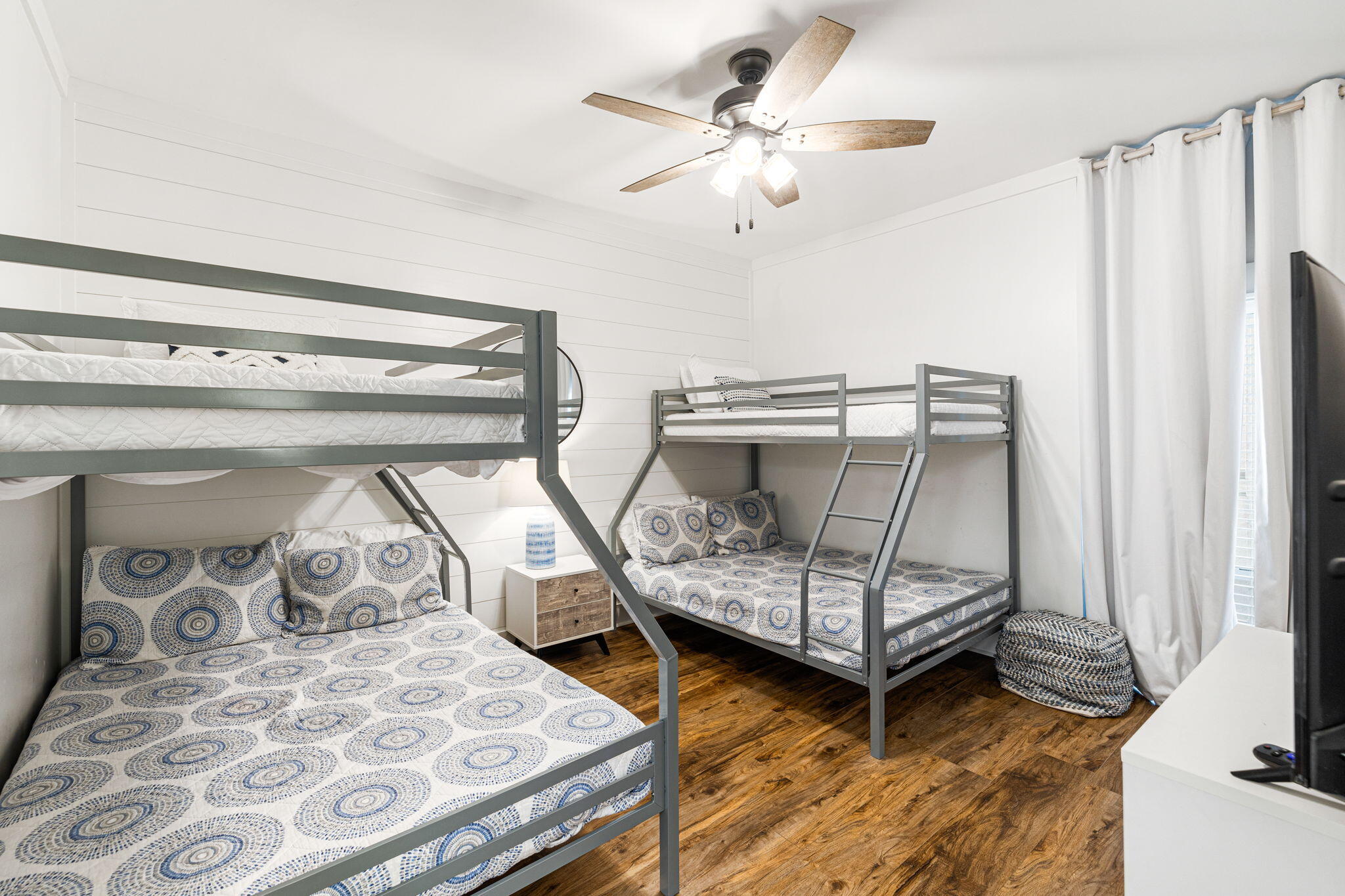 Bedroom with two gray bunk beds, blue-and-white patterned bedding, white shiplap walls, and wood floors.