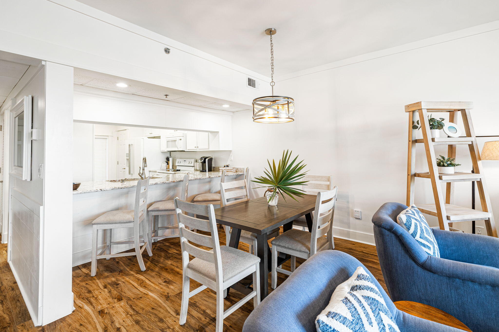 Dining area with a dark wood table, light chairs, and an open white kitchen.