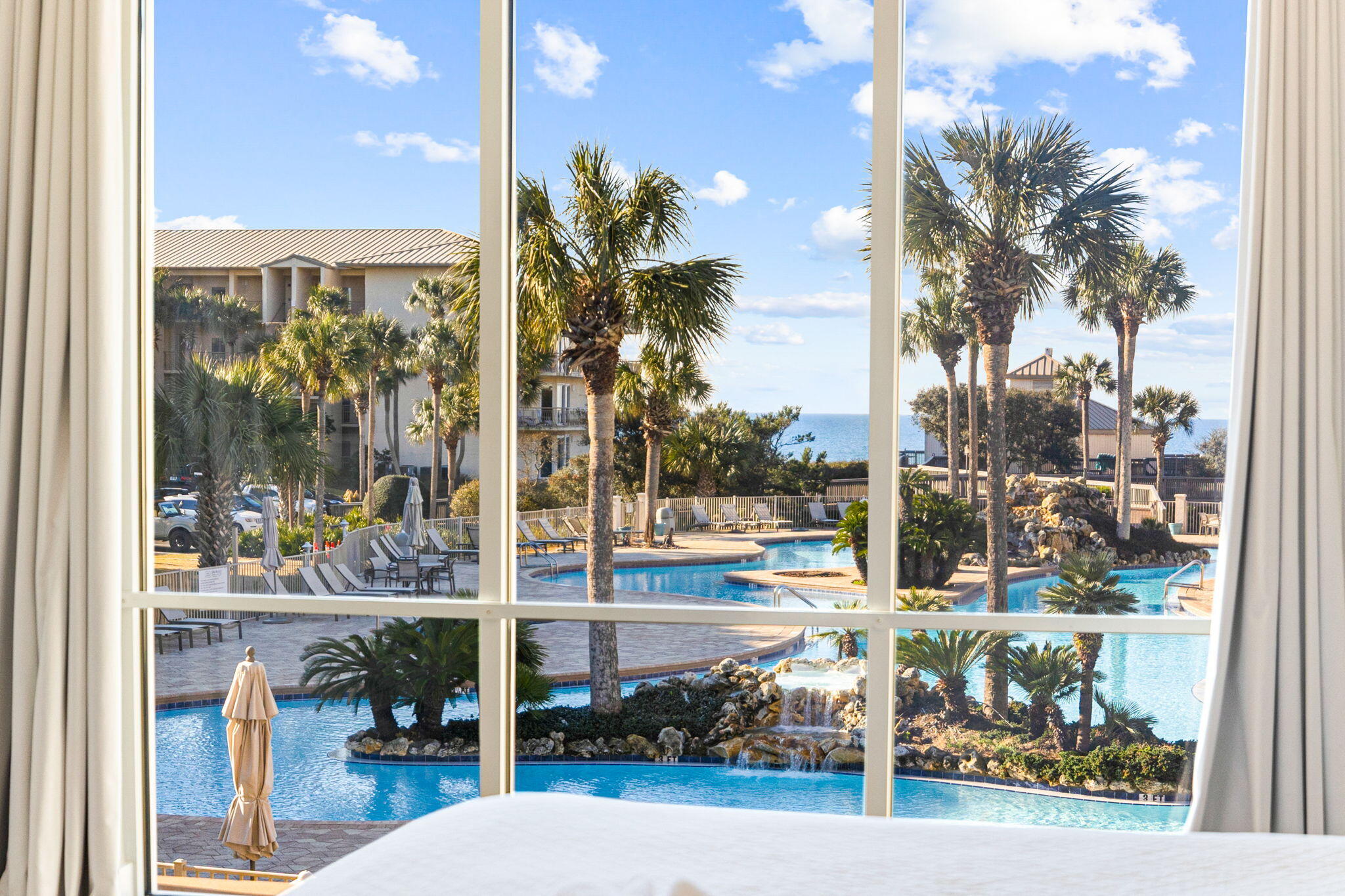 Resort pool and palm trees seen through a window, with the ocean visible beyond.
