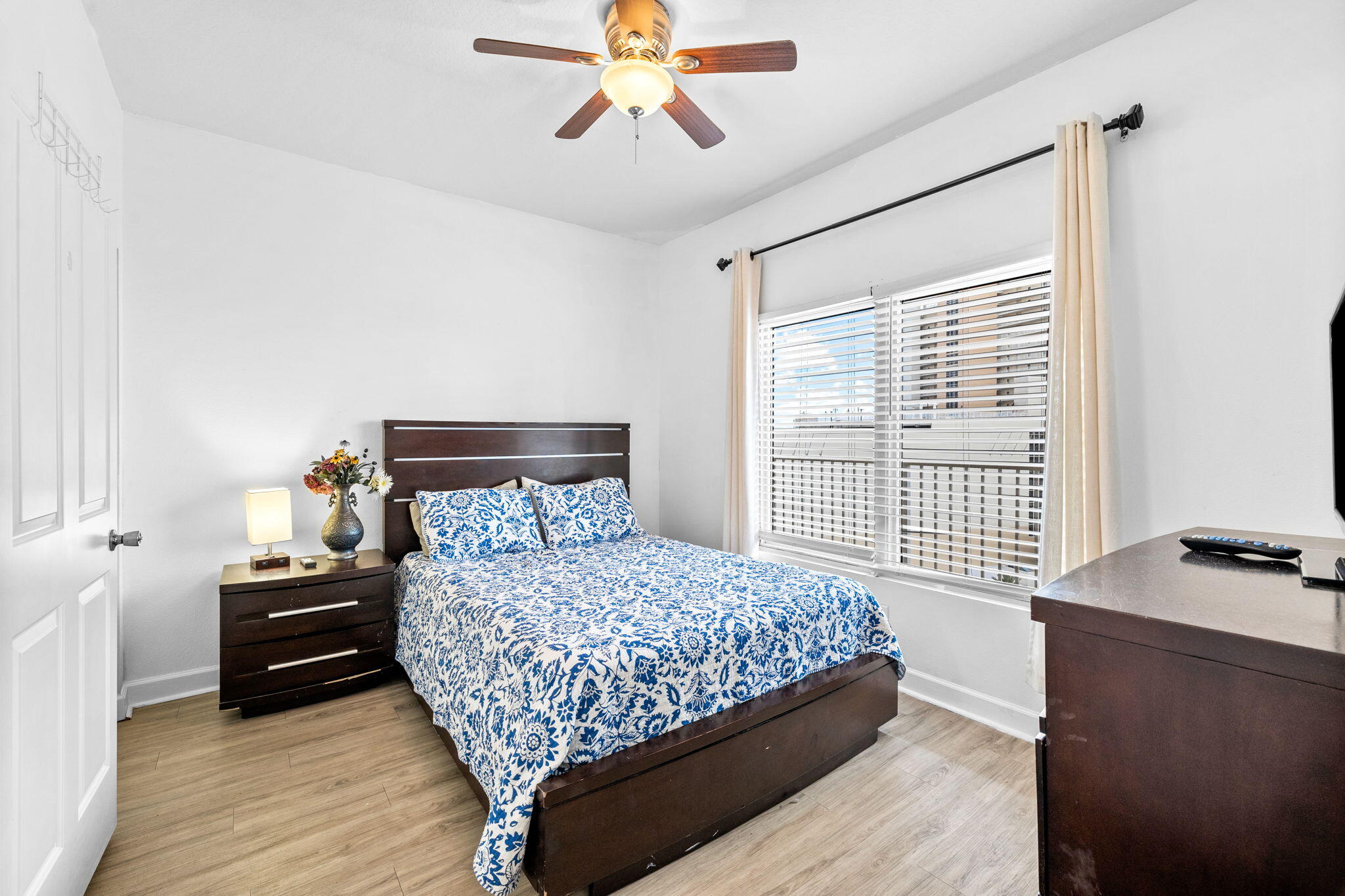 Bedroom with blue-and-white floral bedding, dark wood furniture, and a curtained window.
