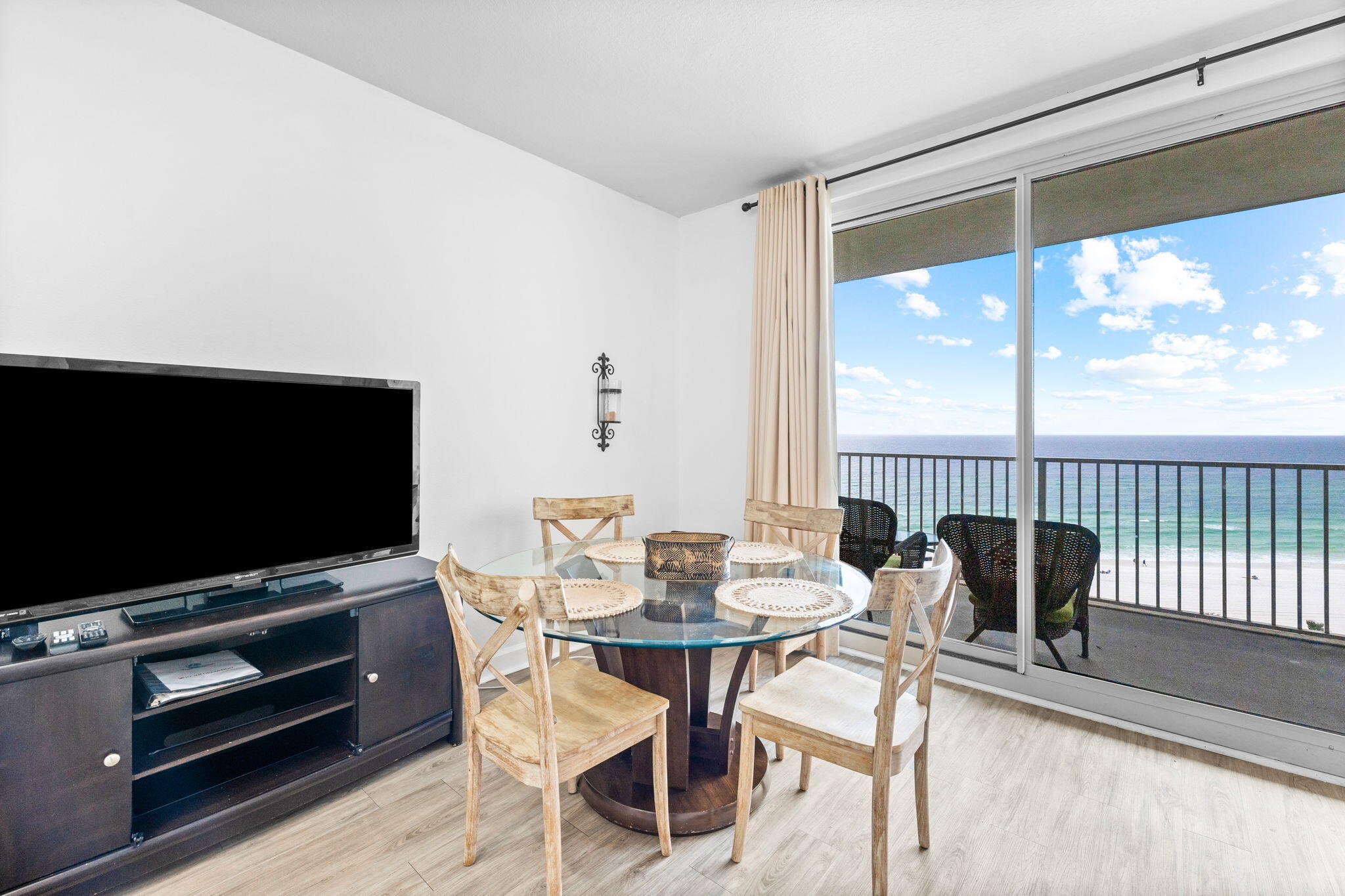Dining area with a round glass table and chairs overlooking the ocean from a balcony.
