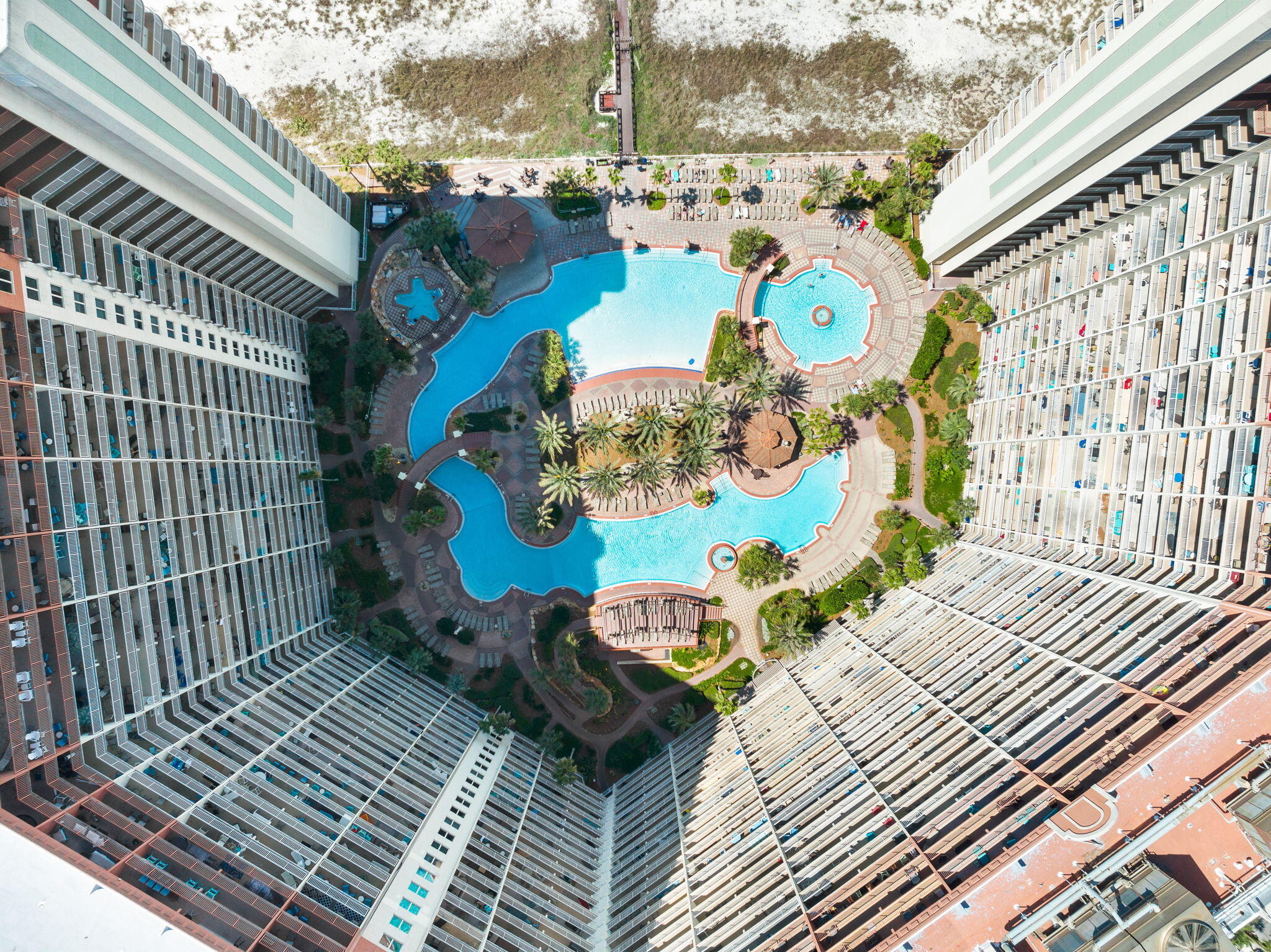 Aerial view of a condominium courtyard with freeform pools, a circular spa, and palm trees.