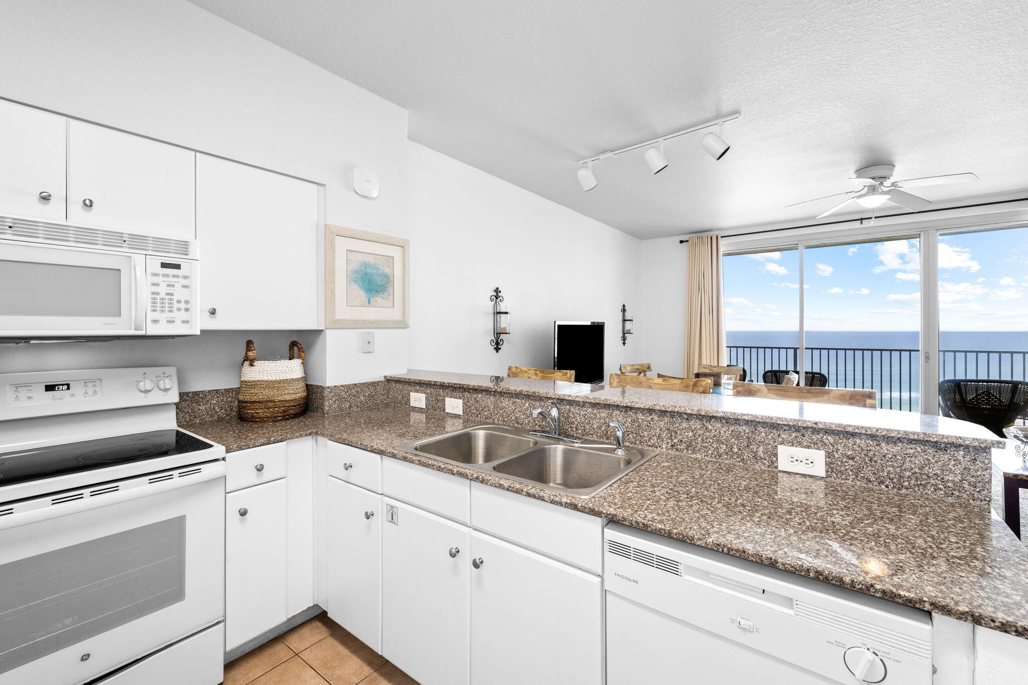 Condo kitchen with granite counters and ocean views through sliding glass doors.