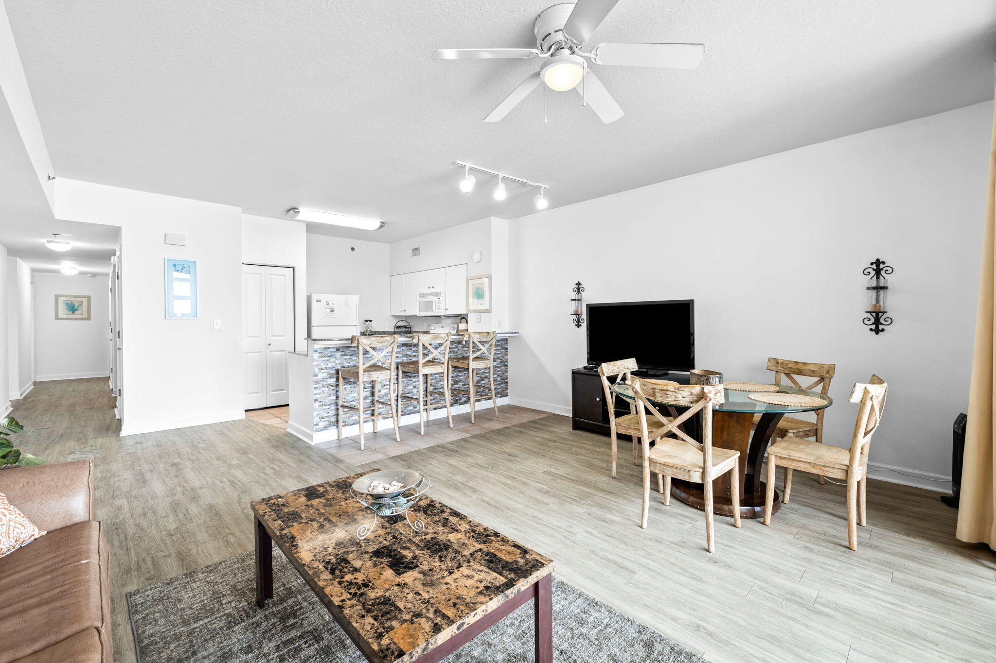 Open-plan condo living and dining area with a mosaic-tile breakfast bar and round glass table.