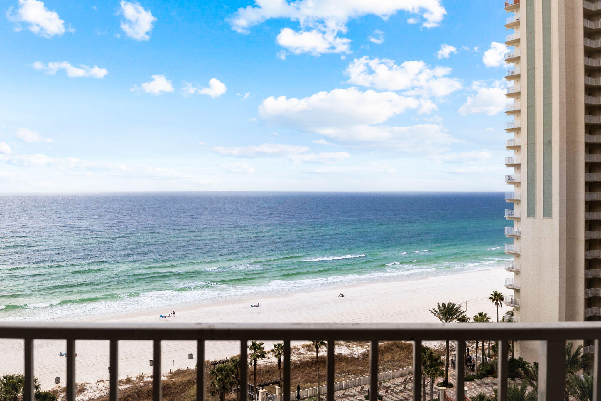 Ocean and beach view from a condo balcony, with a neighboring beachfront tower at right.