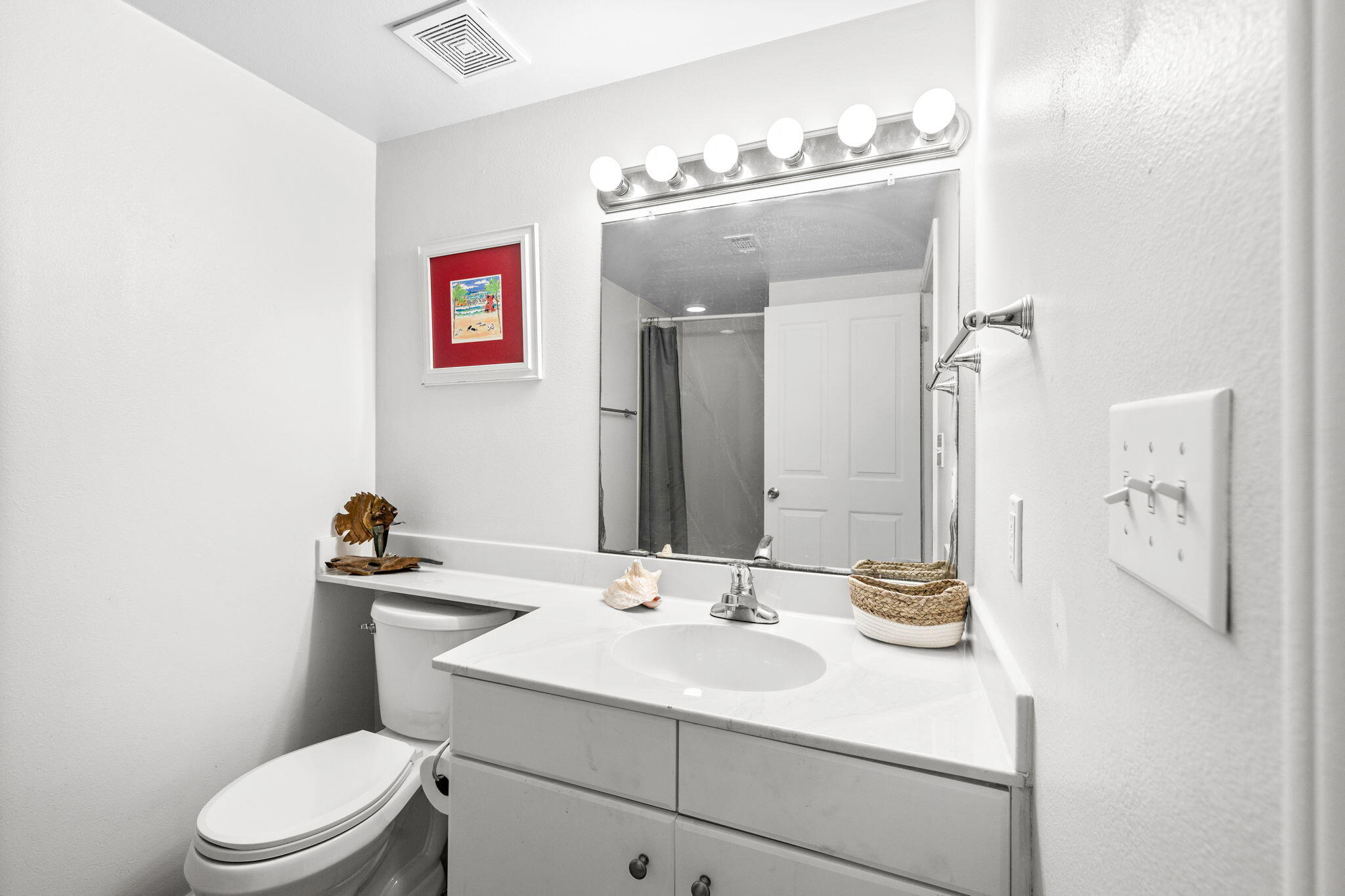Bathroom with a white vanity, illuminated mirror, toilet, and shower with a dark curtain.