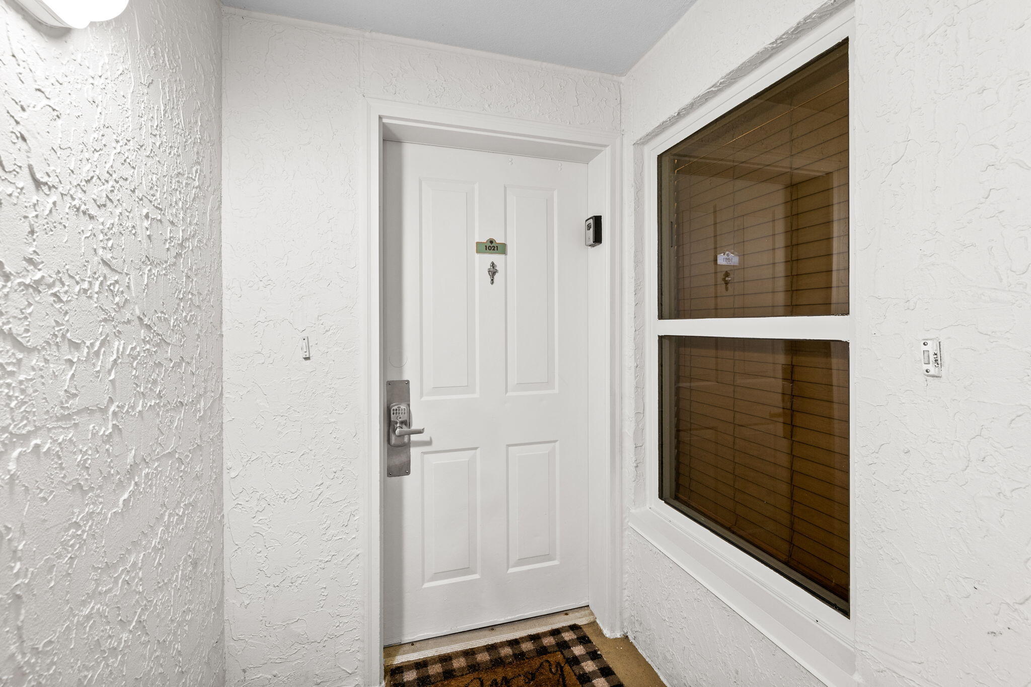 Condominium unit 1021 entry door with a keypad lock and window with wooden blinds.