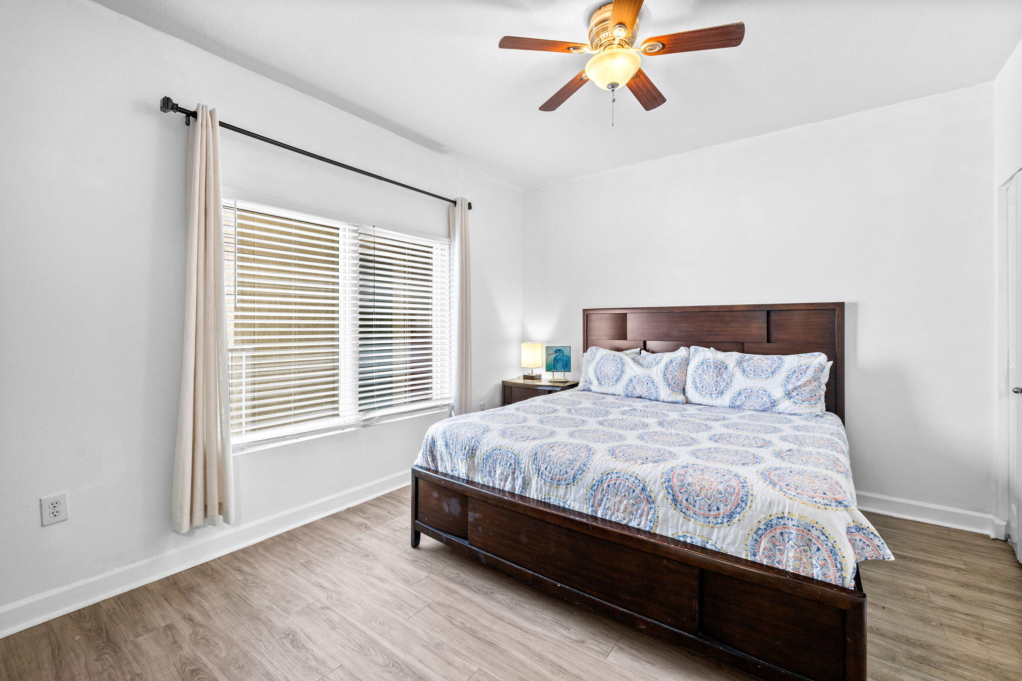 Bedroom with a dark wood bed, blue patterned bedding, and a large window with blinds.