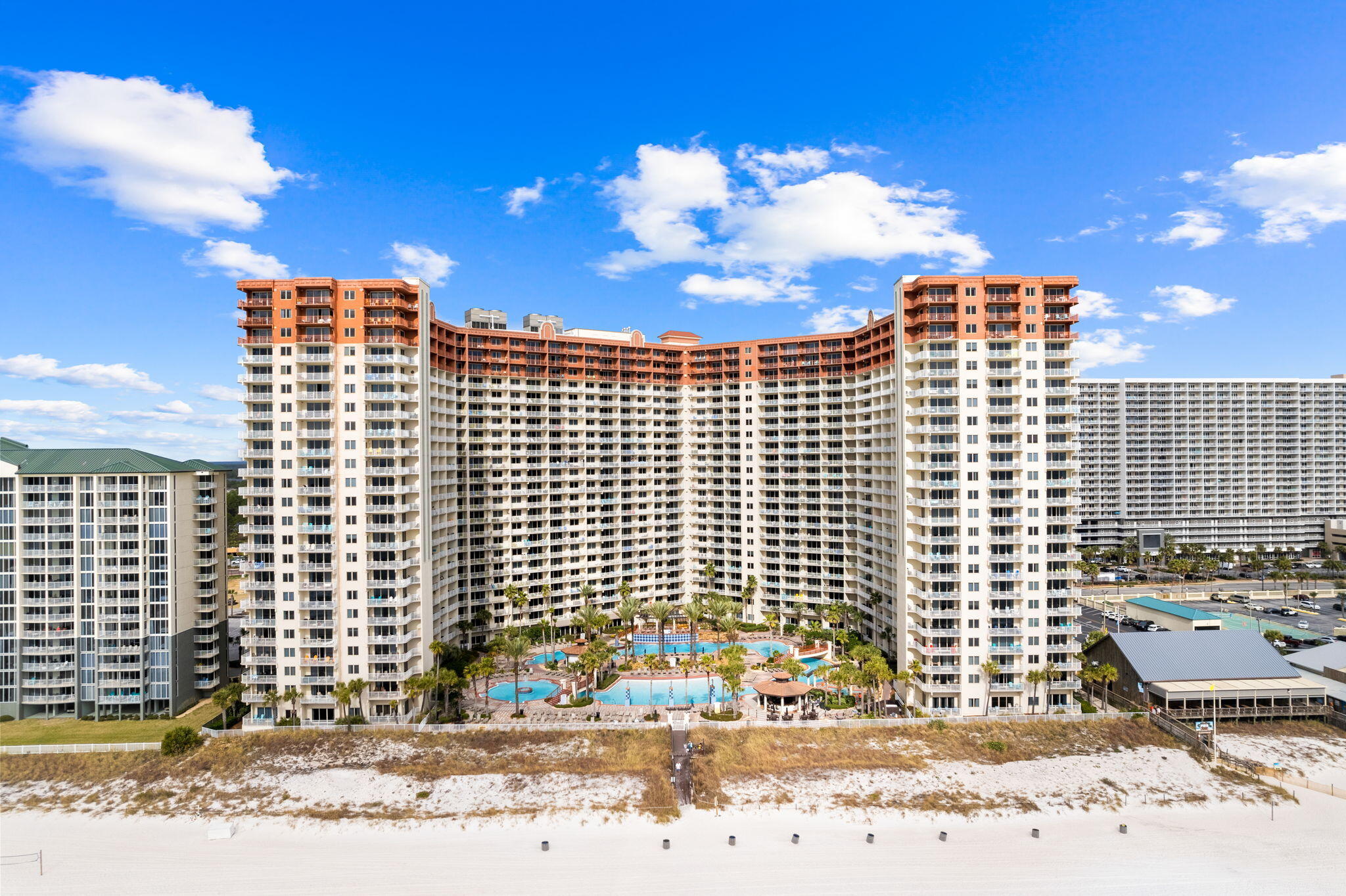 Beachfront condominium complex with multiple pools and balconies, viewed from above.