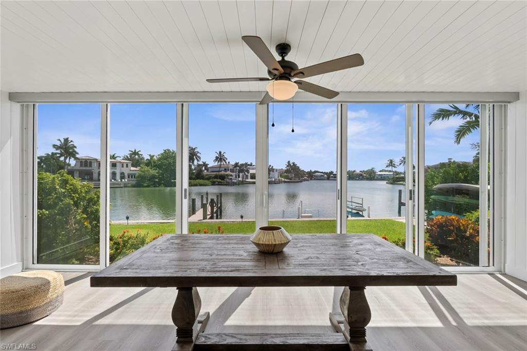 Dining area with a wood table and ceiling fan overlooking a palm-lined waterfront canal.
