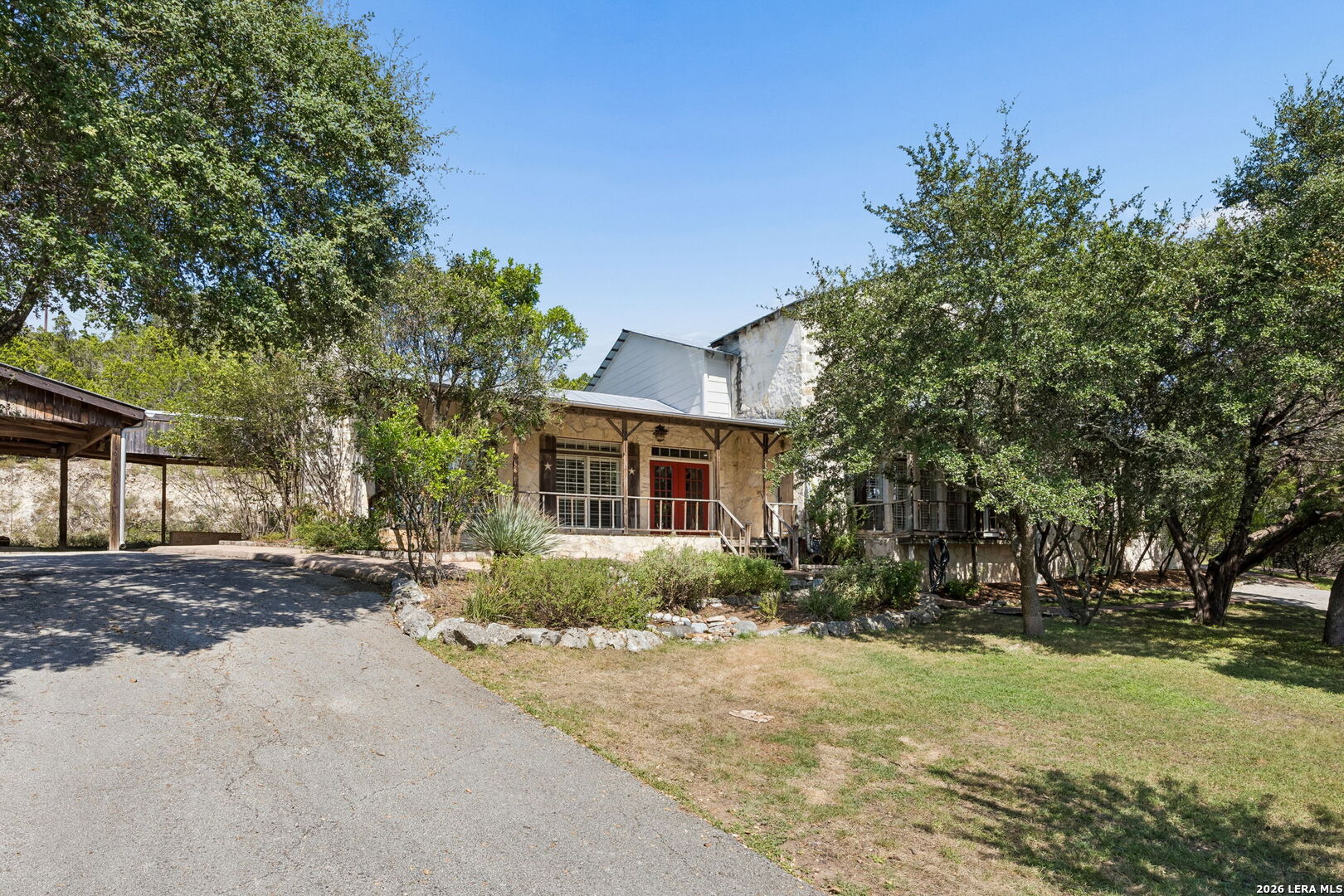 Stone house with red front doors and a covered porch, partly shaded by mature trees.