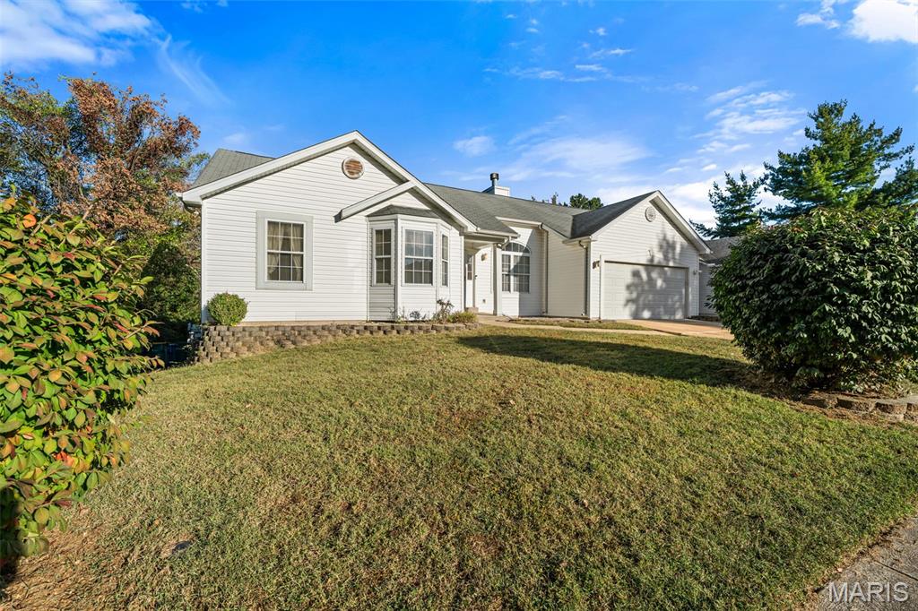 White single-story home with attached garage, broad lawn, and mature landscaping.