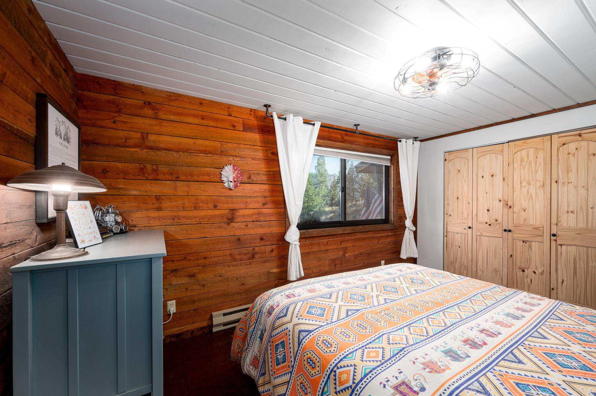 Bedroom with colorful geometric bedding, wood-plank walls, and light pine closet doors.