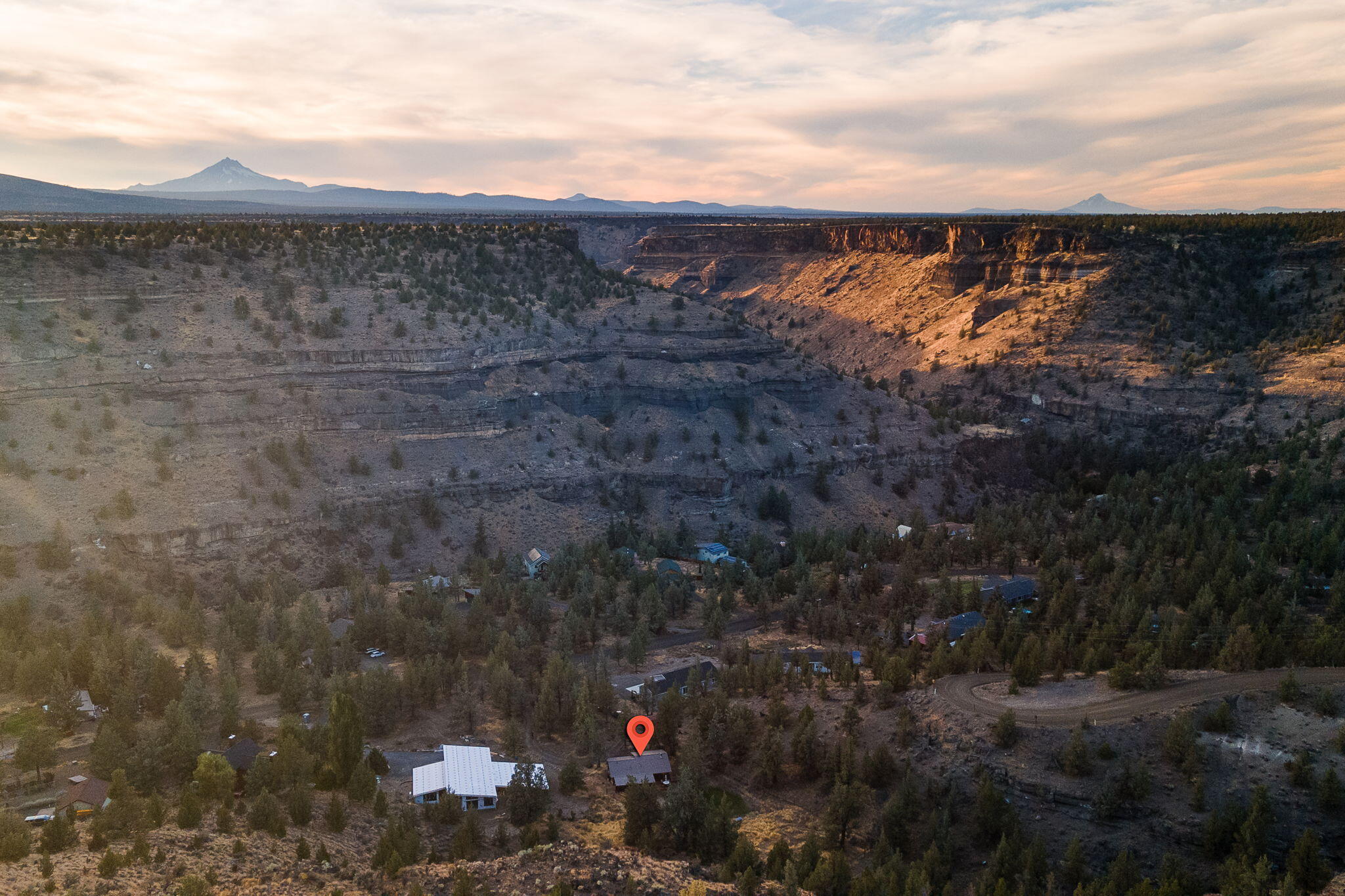 Aerial view of a home beside a deep canyon, with distant mountains in warm evening light.