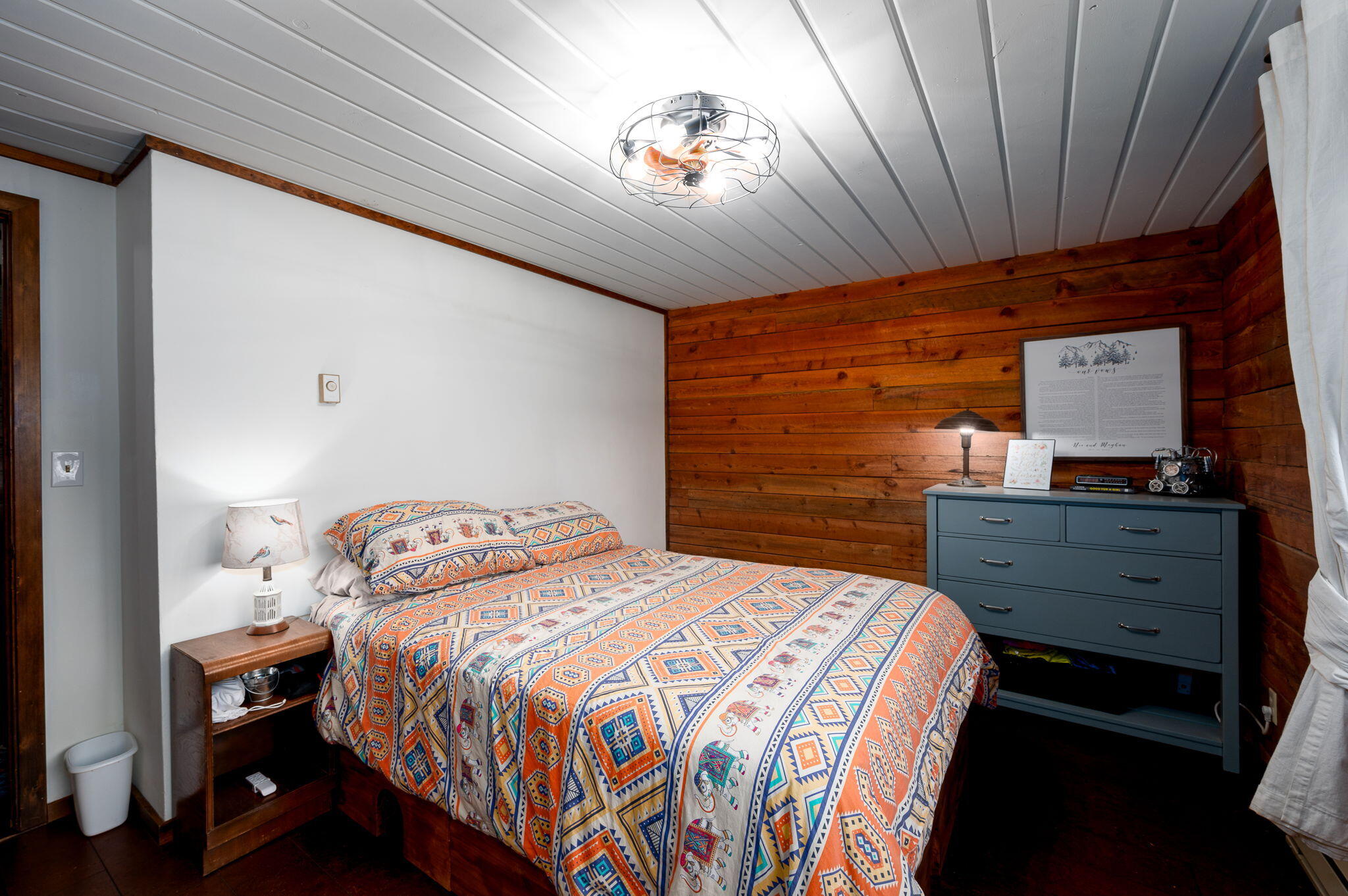 Bedroom with colorful patterned bedding, a wood-plank accent wall, and a blue dresser.