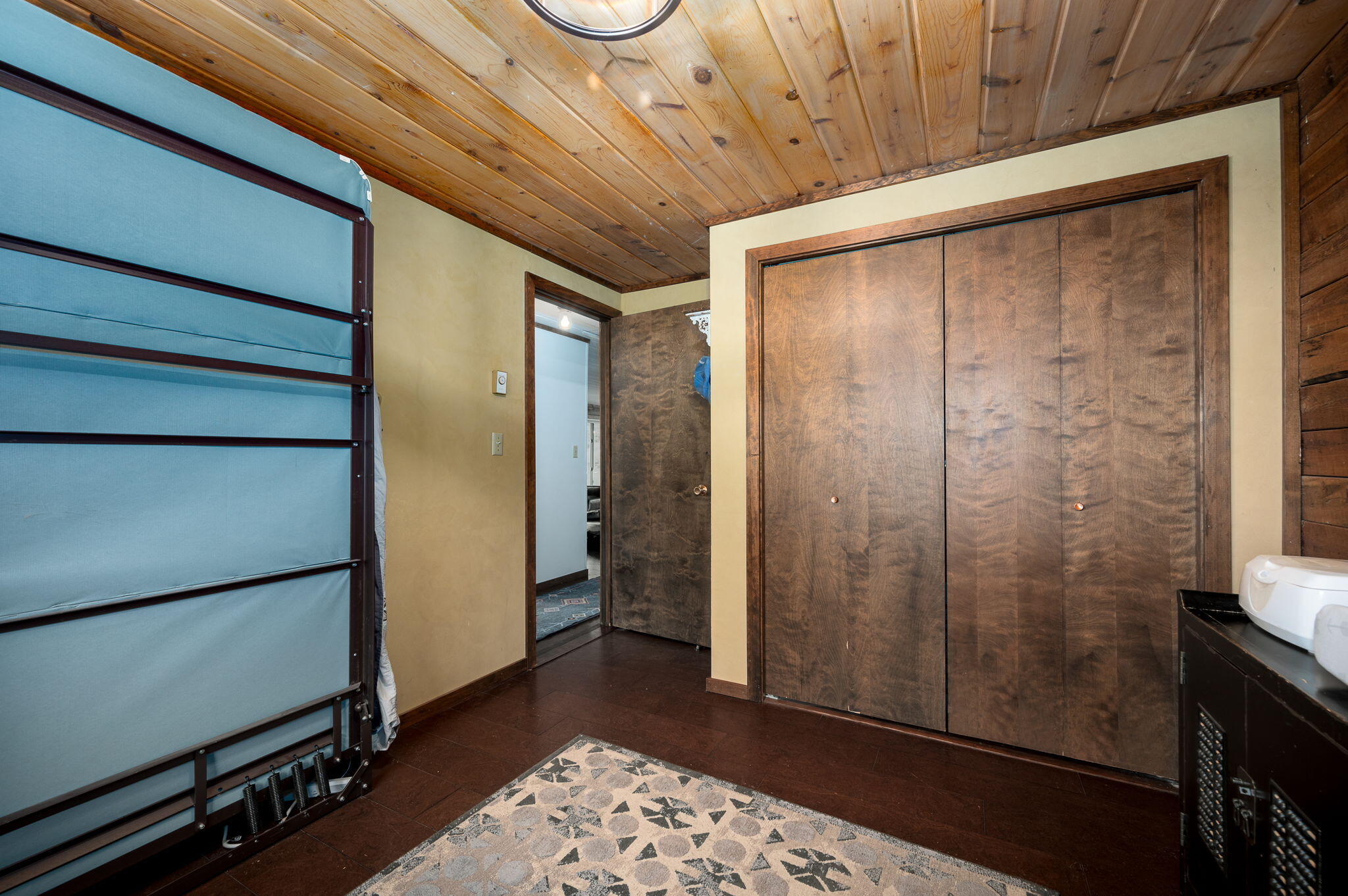 Room with a stowed Murphy bed, large wooden closet doors, and a wood-plank ceiling.