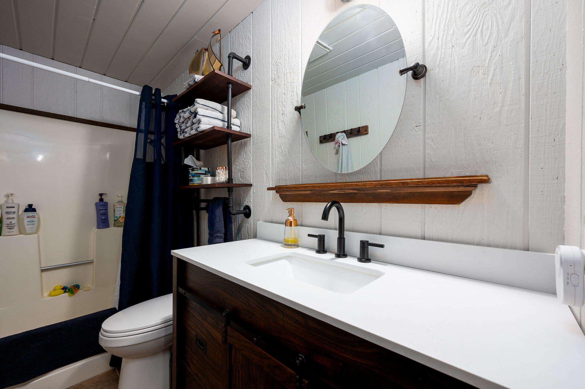 Bathroom with a dark wood vanity, oval mirror, and tub-shower with a navy curtain.