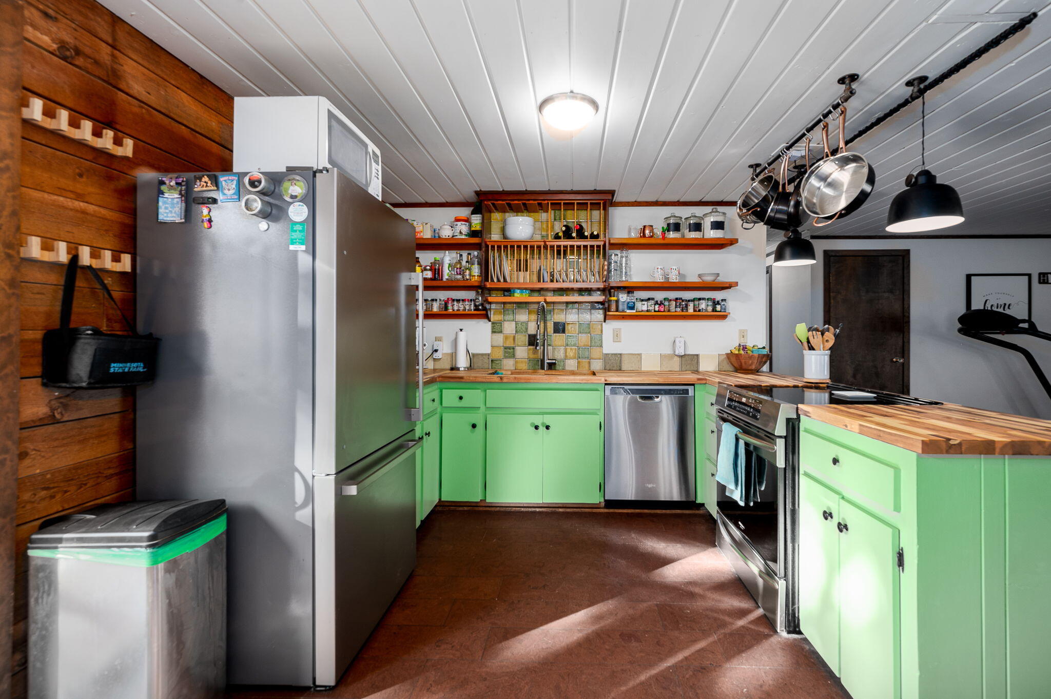 Kitchen with bright green cabinets, butcher-block counters, stainless steel appliances, and hanging pots.