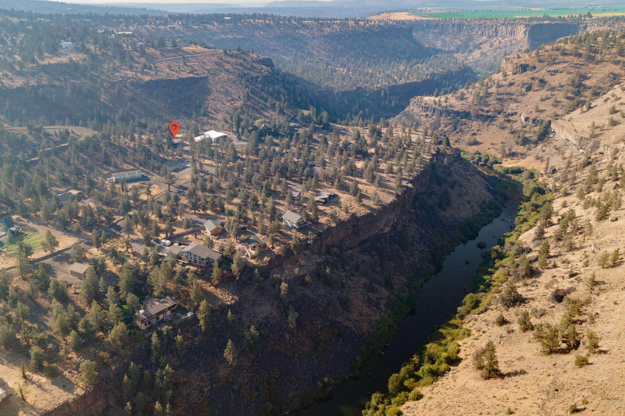 Aerial view of a canyon-side property marked by a red pin, with scattered homes and a river below.
