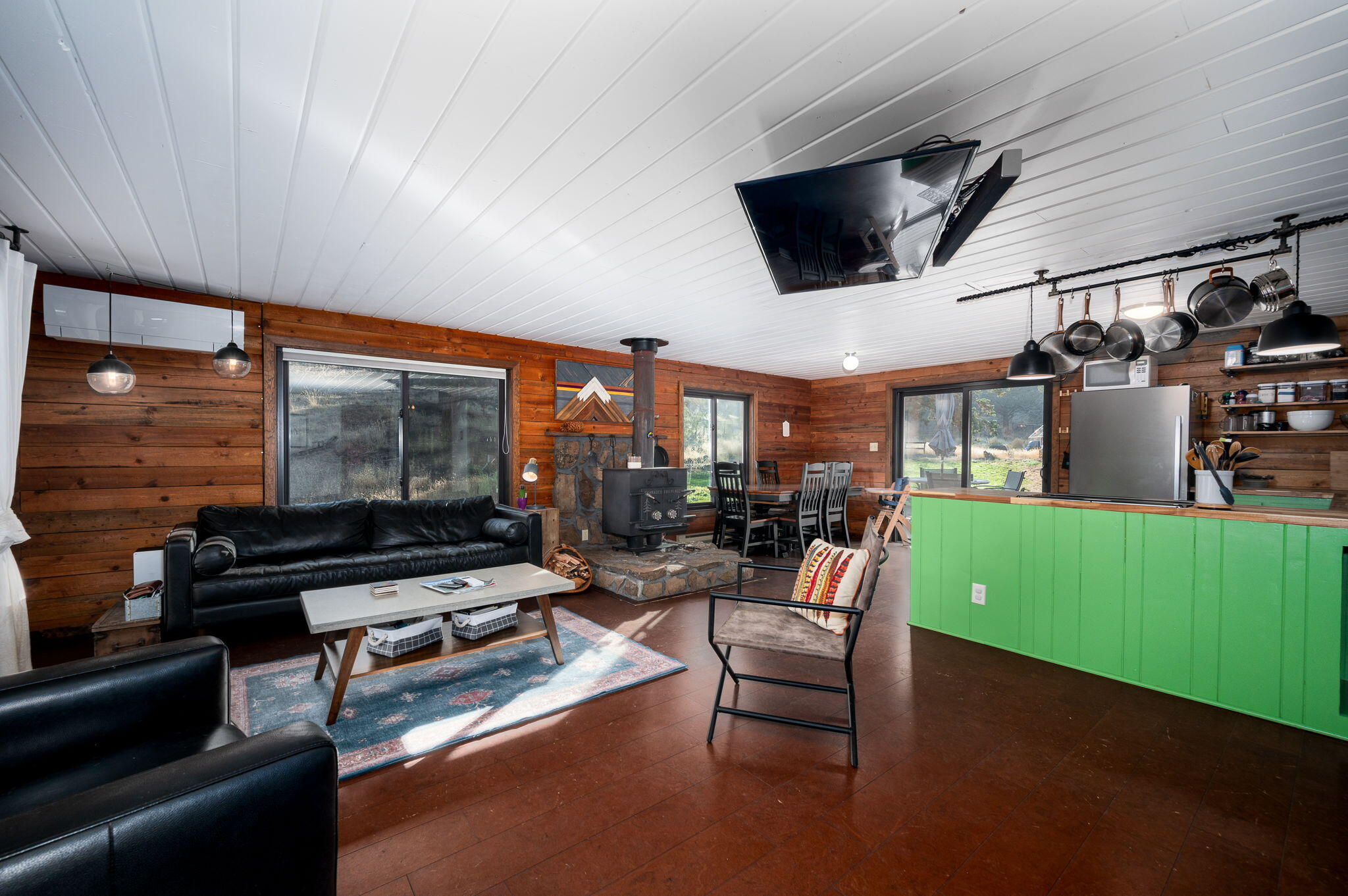 Open-plan living room and kitchen with wood stove, wood-paneled walls, and a bright green island.