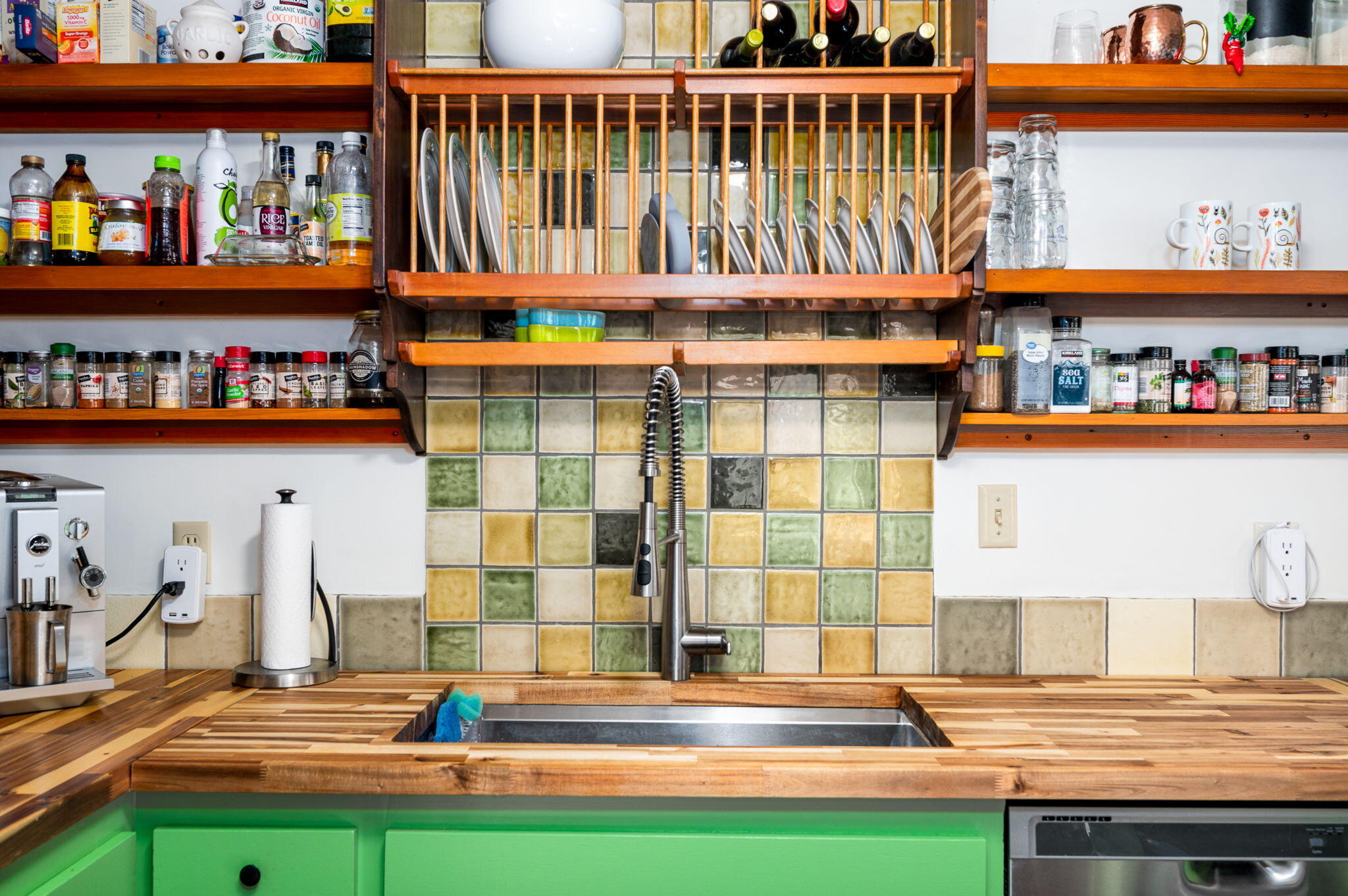Kitchen sink with a spring-coil faucet, colorful tile backsplash, and open shelves stocked with dishes and spices.