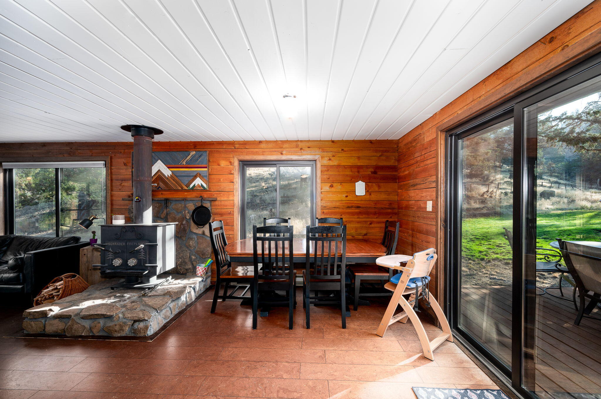 Wood-paneled dining area with a stone-hearth wood stove and sliding doors opening to a lawn.