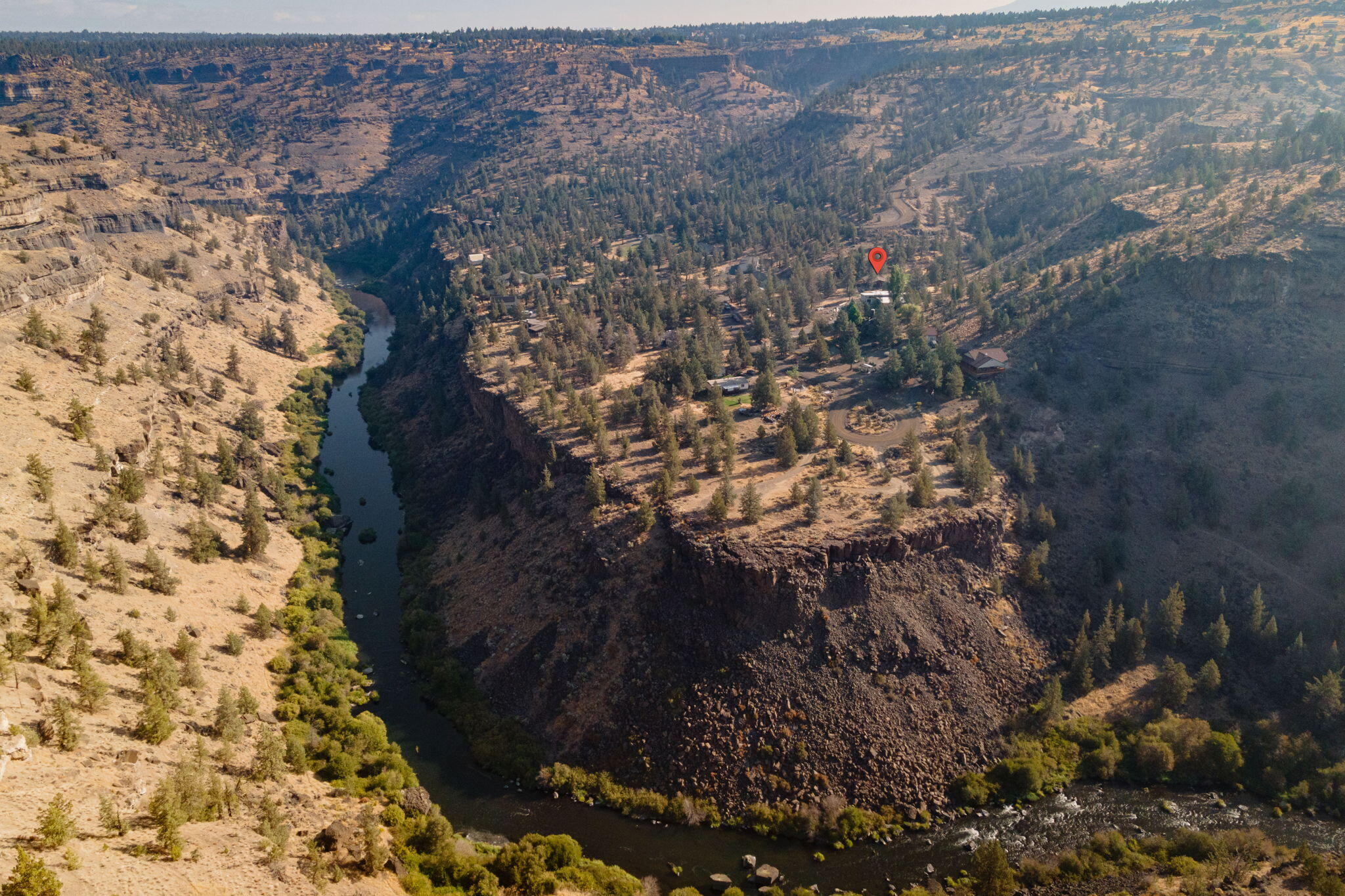 Aerial view of a river canyon, with homes on the wooded plateau and a red map pin marking a property.