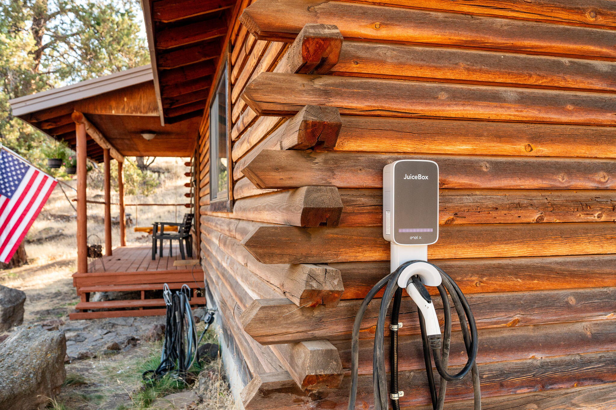 Log cabin exterior with a JuiceBox EV charger beside a covered porch and American flag.